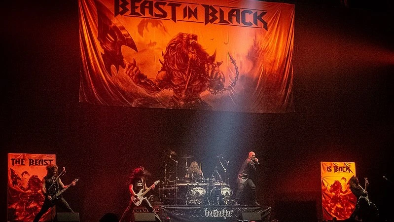 A dynamic metal band performing onstage, with intense lighting and a backdrop featuring fierce beast-themed artwork.