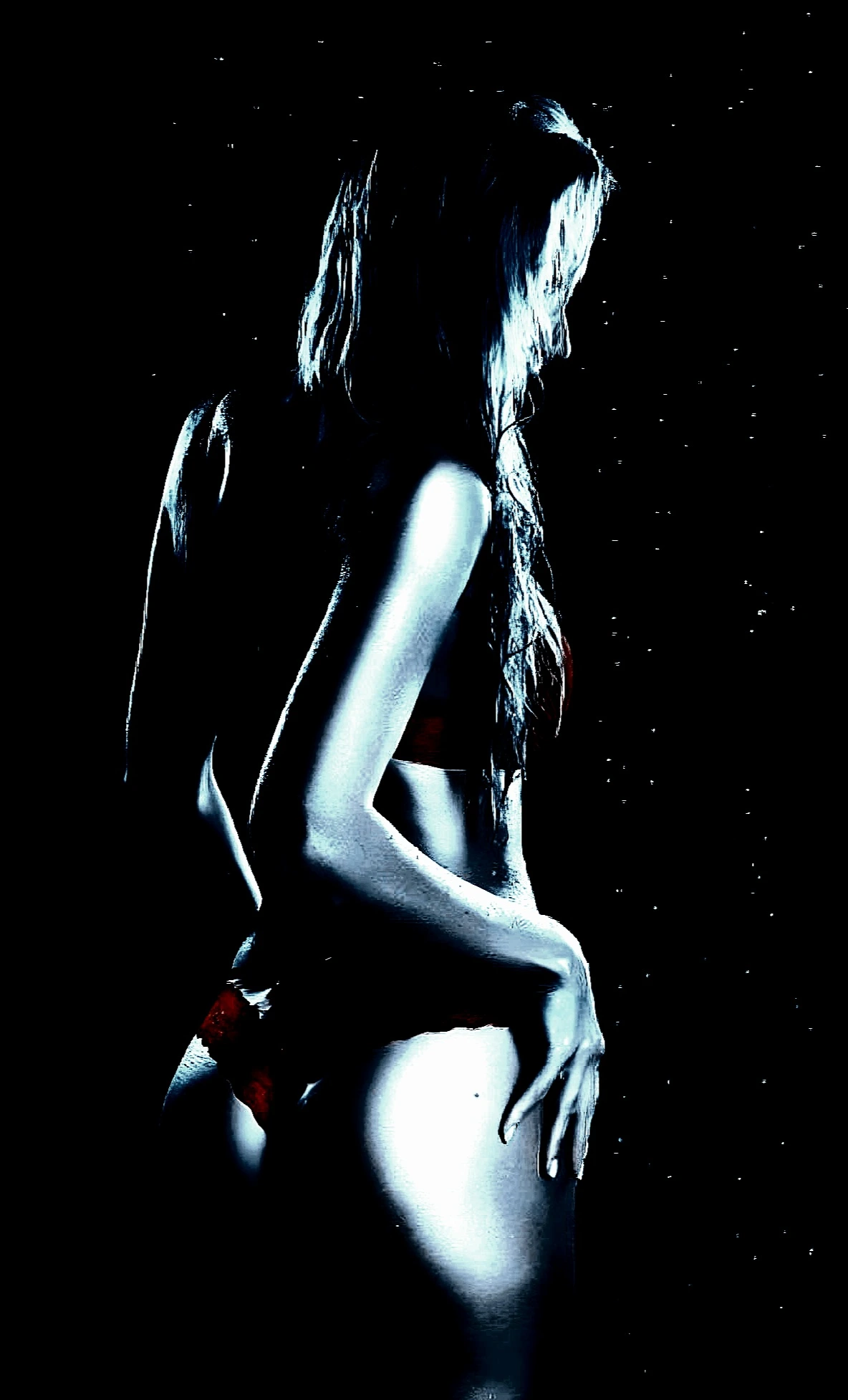 Side view of a woman in a dimly lit setting, highlighting her silhouette and wearing a bikini against a dark background with a hint of sparkle.