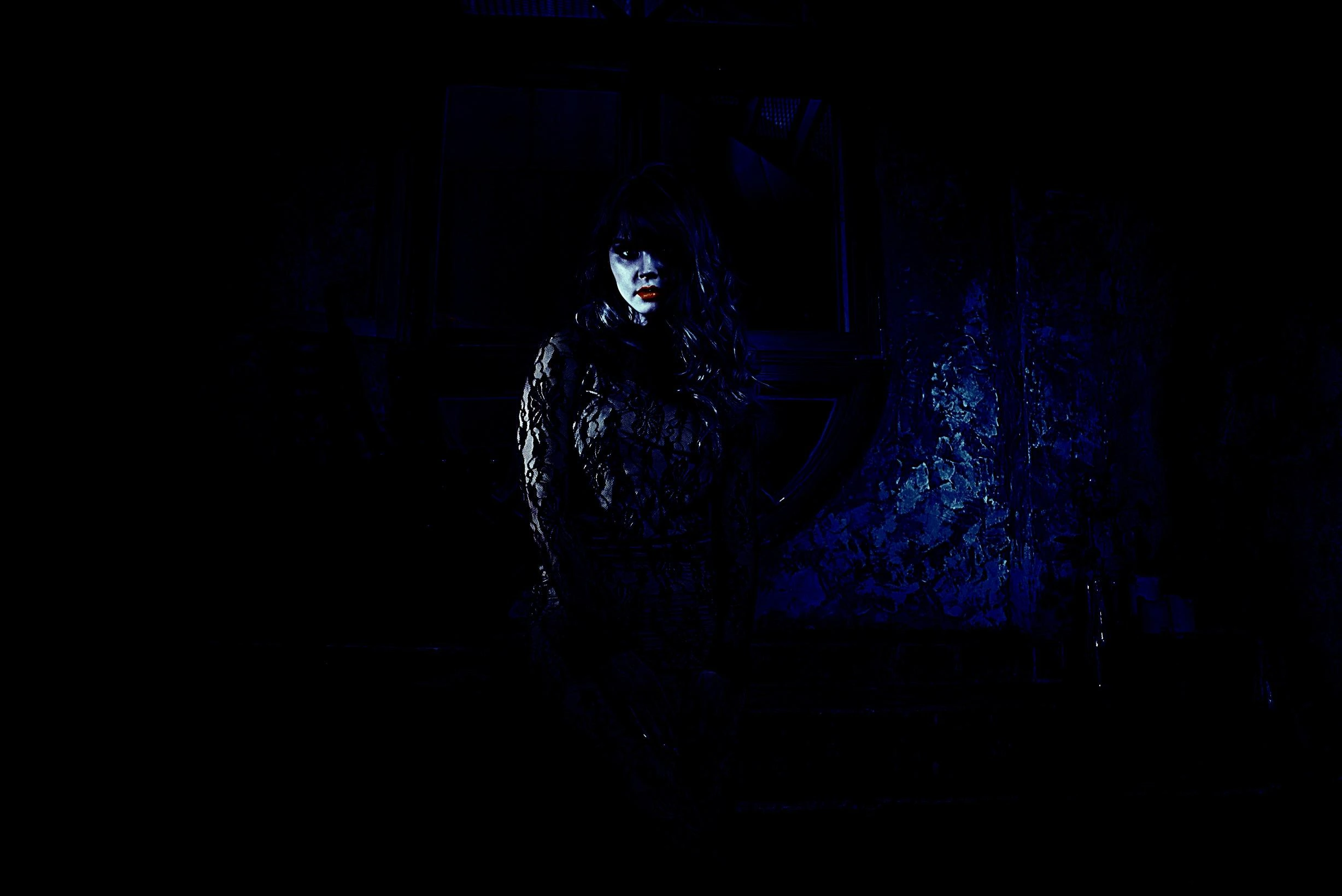 Woman with dark makeup in a gothic outfit, posed in a shadowy forest, highlighting an eerie yet elegant vibe.