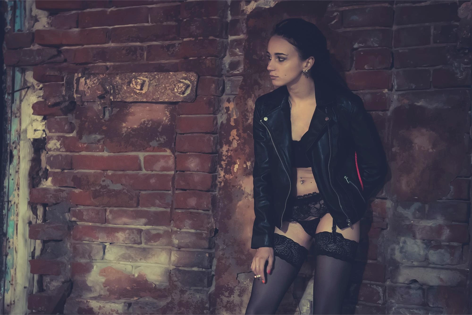 Woman in a black leather jacket and lace lingerie leaning against a rustic brick wall, gazing into the distance. Close-up of a woman wearing a black leather jacket, mini skirt, and fishnet stockings, leaning against a wall. Woman in black lace lingerie standing in a cozy bedroom with exposed brick walls, illuminated by warm lights. Woman in black lingerie lying on a bed in a softly lit bedroom with exposed brick walls, looking at the camera. Woman in black lace outfit standing in an underground parking lot, illuminated by car headlights in the background. Woman in black sheer lingerie reclining on a bed, with a large mirror reflecting her in the background. Woman in sunglasses holding a cocktail glass at a dimly lit bar, wearing red lipstick and a mysterious expression. Woman in fishnet stockings and high heels leaning against a wall in a dimly lit urban tunnel, lost in thought.