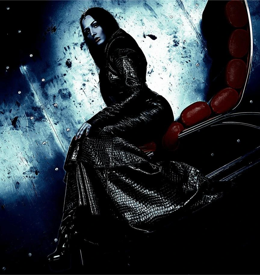 Woman in a black, form-fitting zip-up latex dress with her hands on her hips, giving a powerful and intense stare in a dark setting.