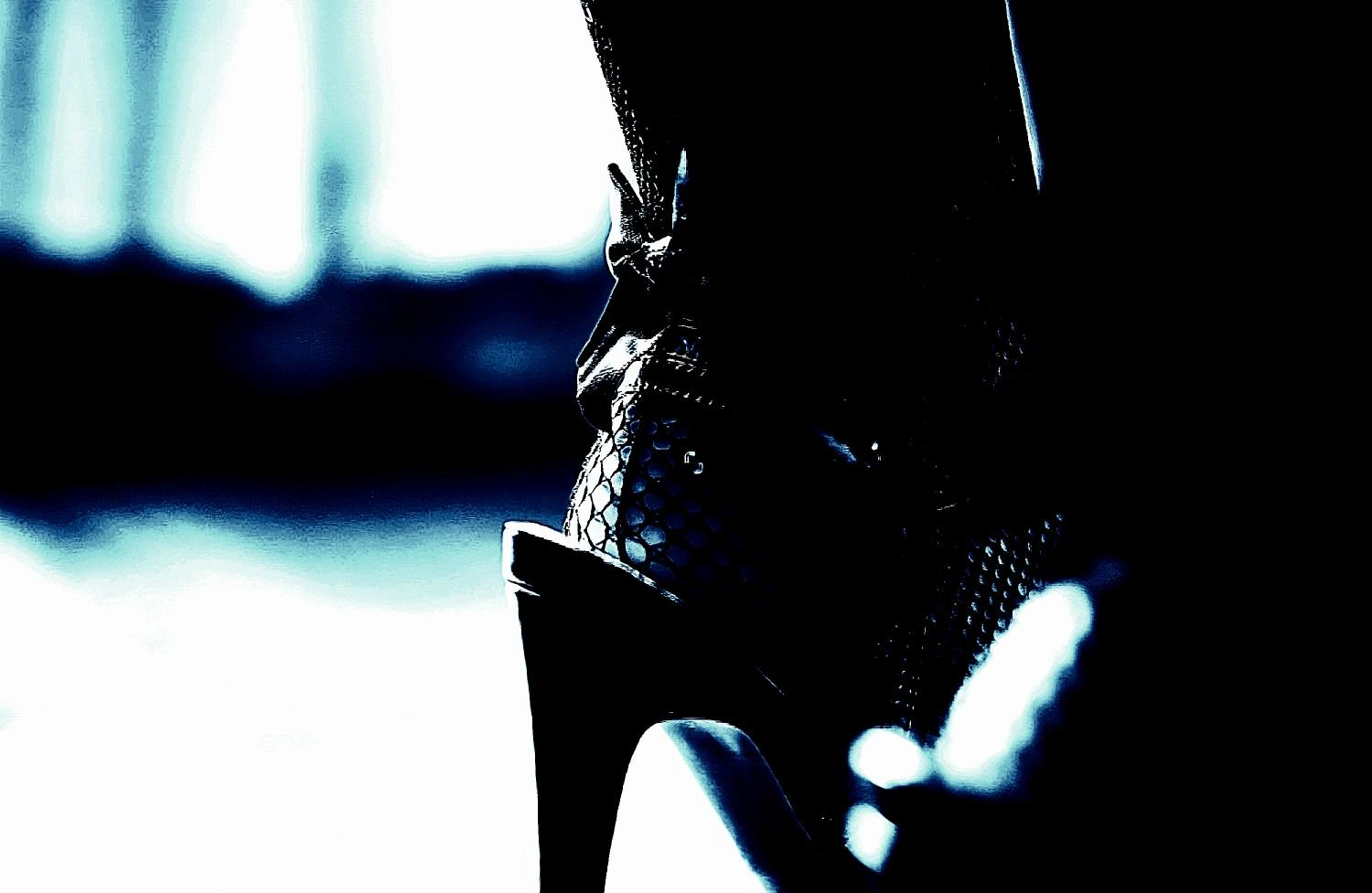 Close-up of a black high-heeled boot with a textured snakeskin pattern against a dark background. 