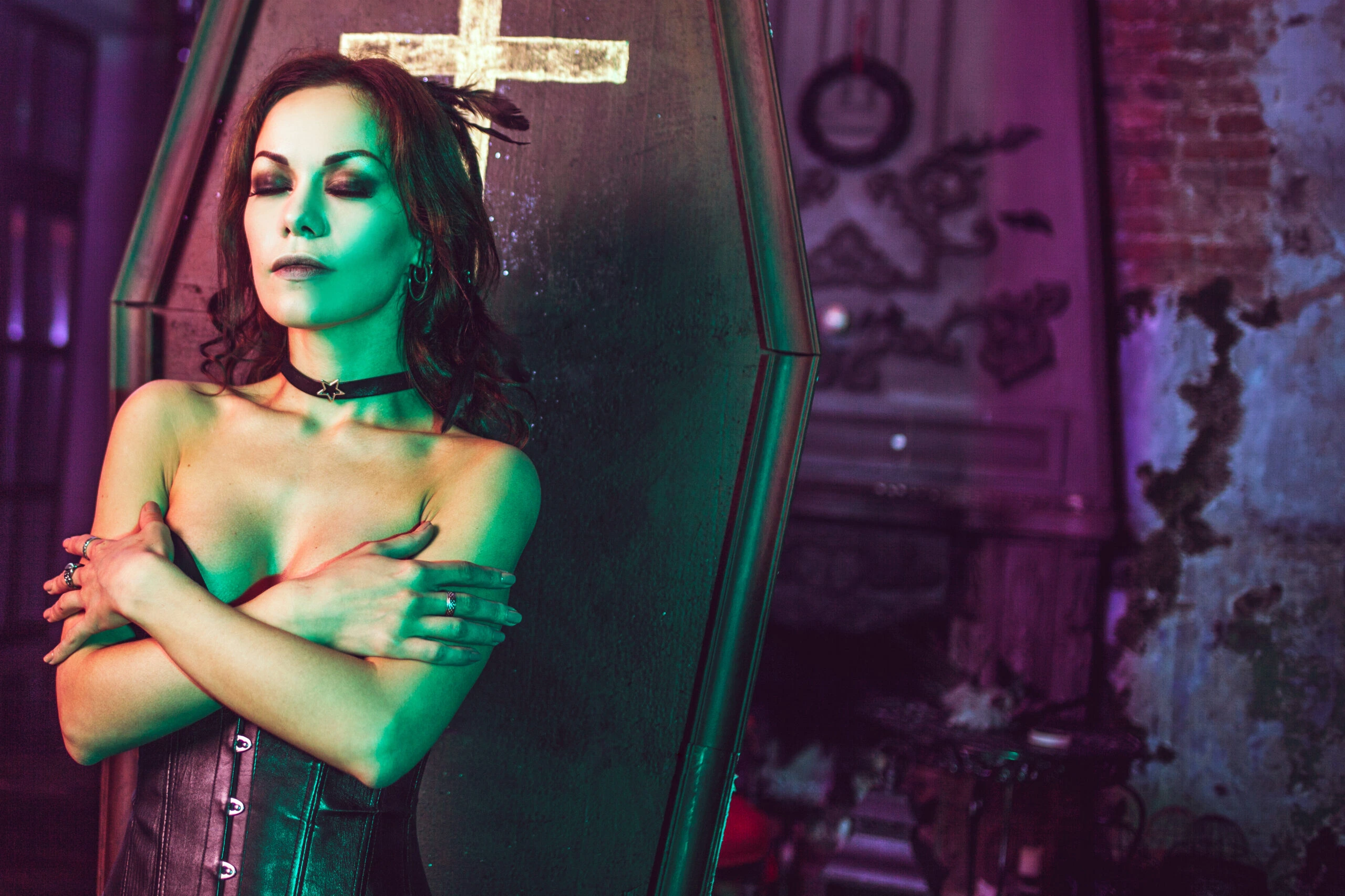 A woman in a gothic ensemble standing against a coffin, conveying a somber elegance in a room of antique decor.