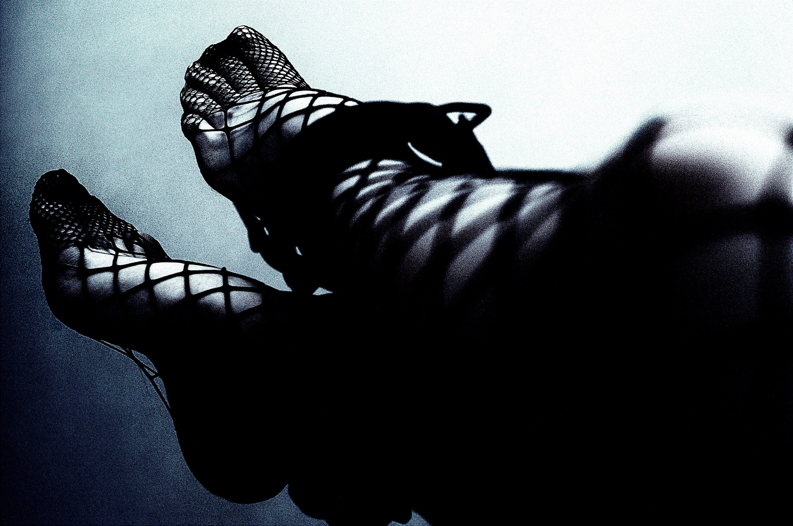 Intense monochrome photo focusing on a person's clasped hands with bondage cuffs, set against a dark background, highlighting themes of control and consent in BDSM play.