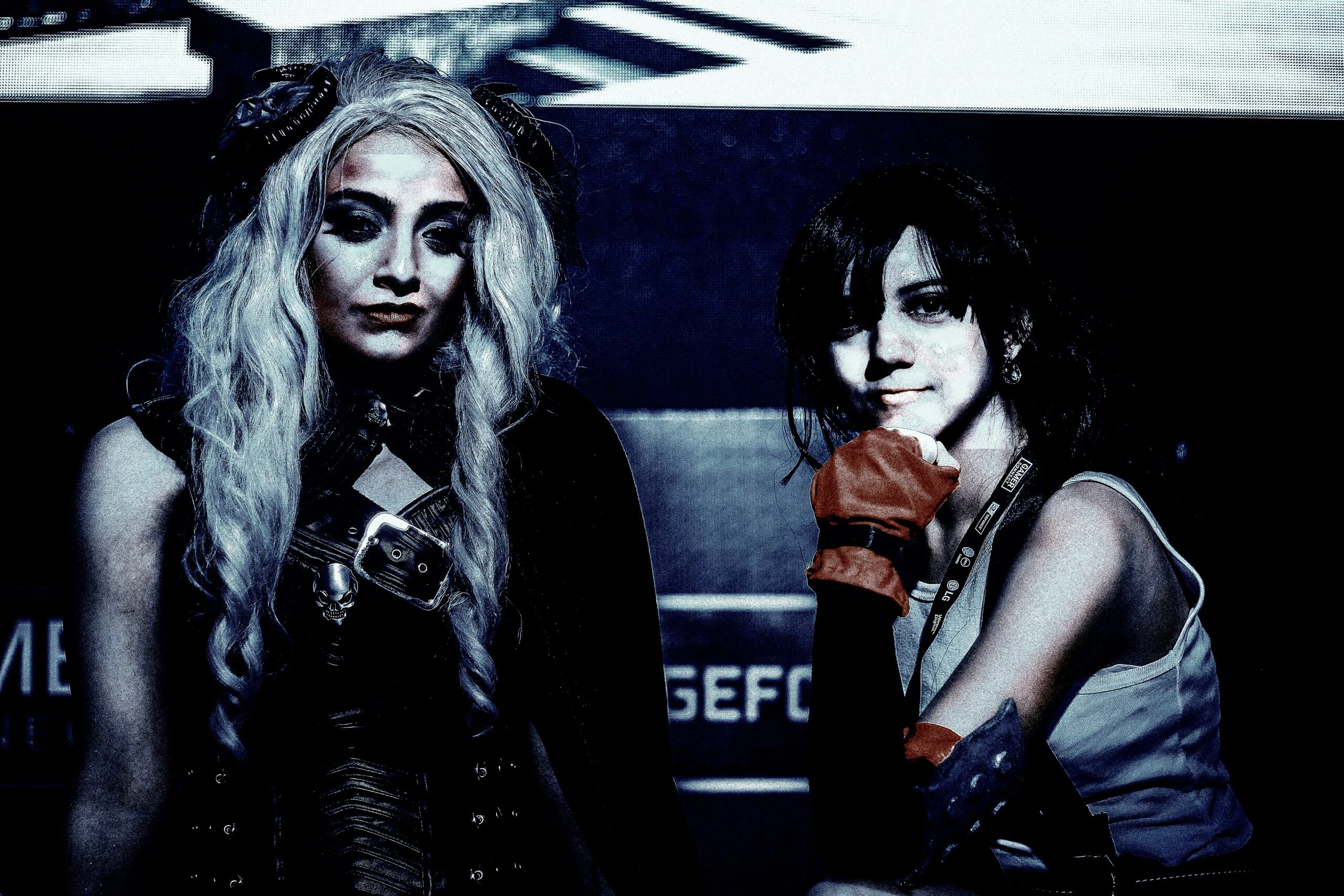Two women in gothic and steampunk attire posing at a gaming event, with heavy blue filters emphasizing the dark aesthetic.