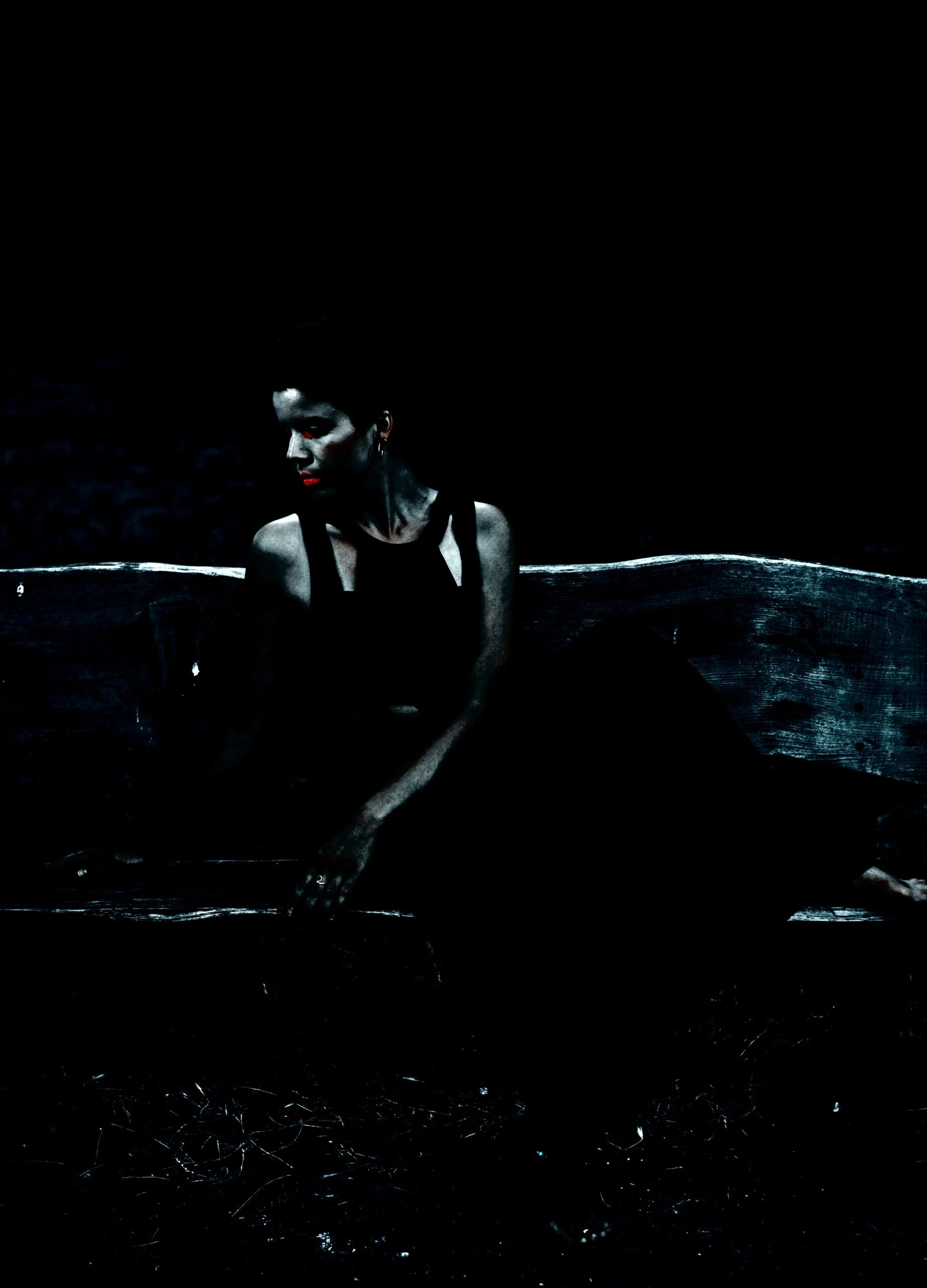 A solitary figure sits on a weathered bench in a desolate setting, draped in dark attire against the stark contrast of the night, evoking a feeling of gothic solitude.
