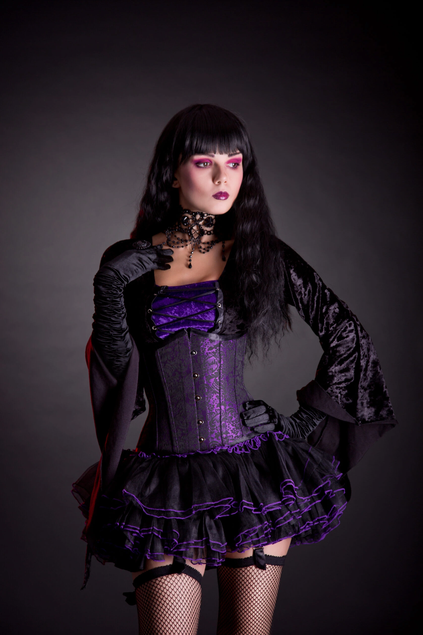 Woman in full gothic regalia holding an ornate black umbrella, her striking makeup, and choker necklace accentuating the dark, romantic aesthetic of her outfit.