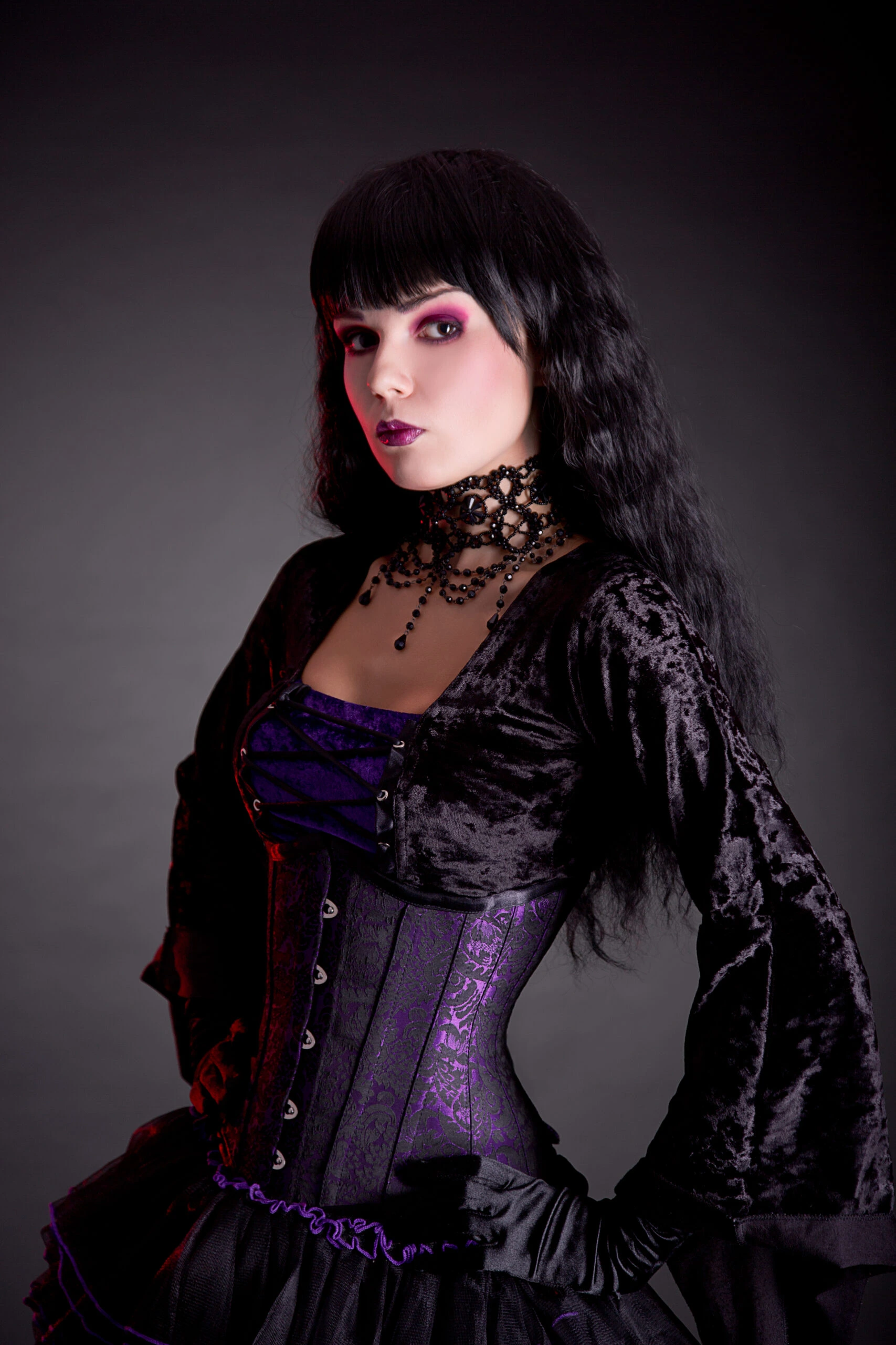Dark romanticism captured with a model in a purple and black velvet gothic corset dress, standing confidently in a smoky ambiance.