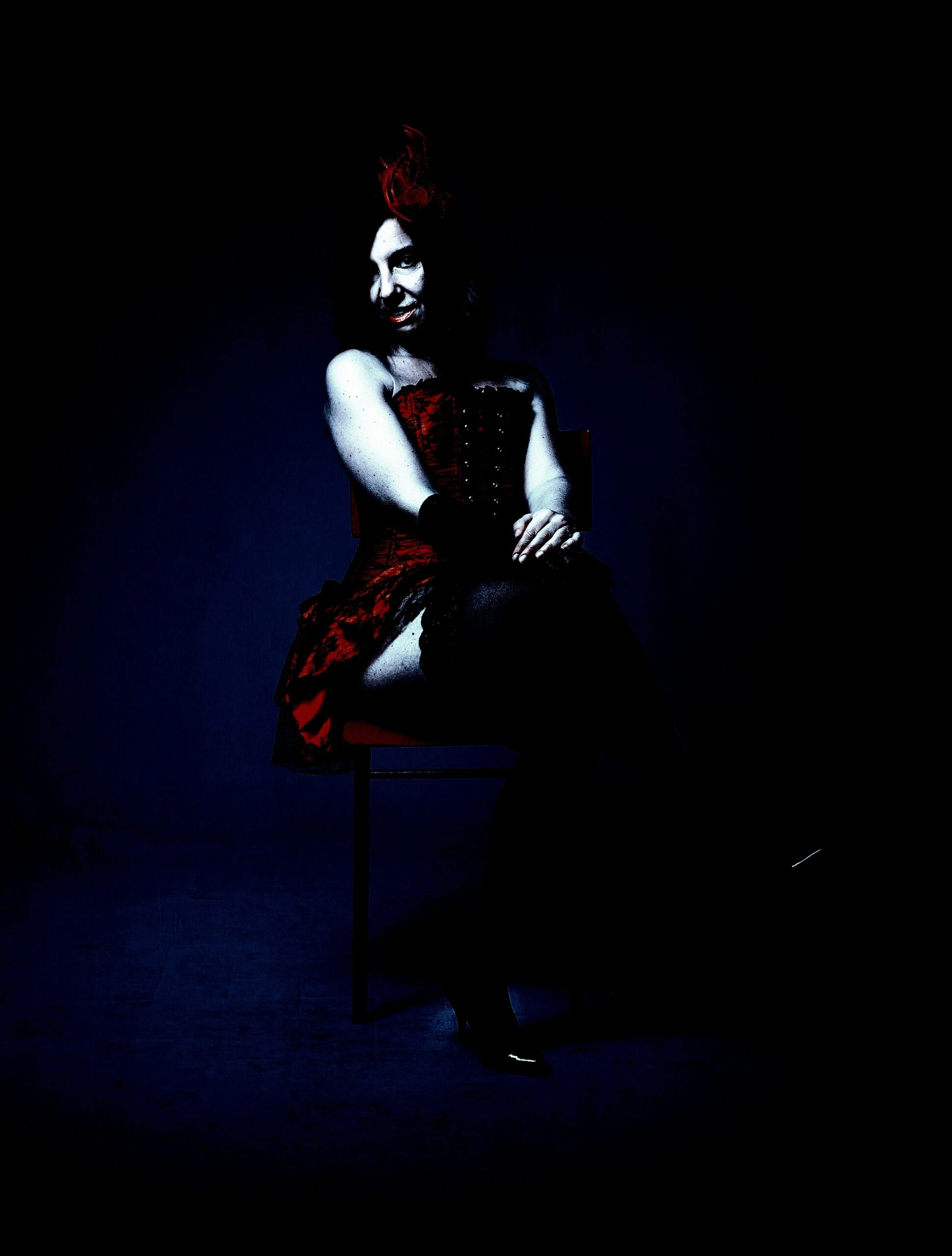 Gothic woman with red hair in an updo, sitting on a chair wearing a dark corseted dress, exuding an aura of dark elegance.