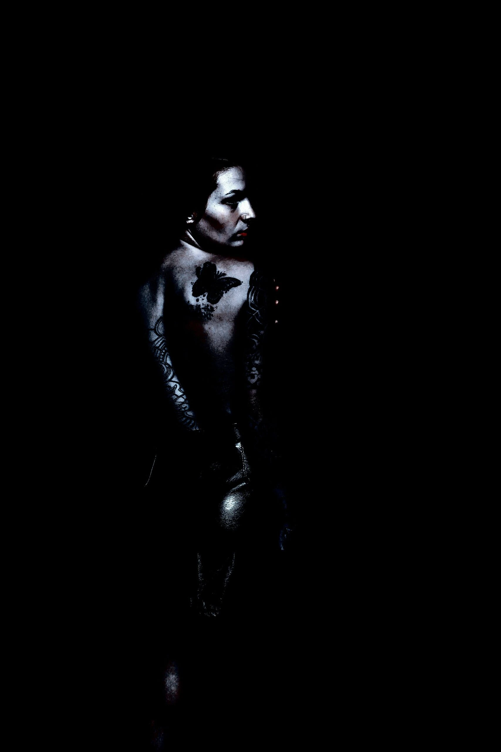 A person with a dark ambiance, featuring a butterfly tattoo on the shoulder and tribal-like patterns on the arm, giving a mysterious goth aesthetic.