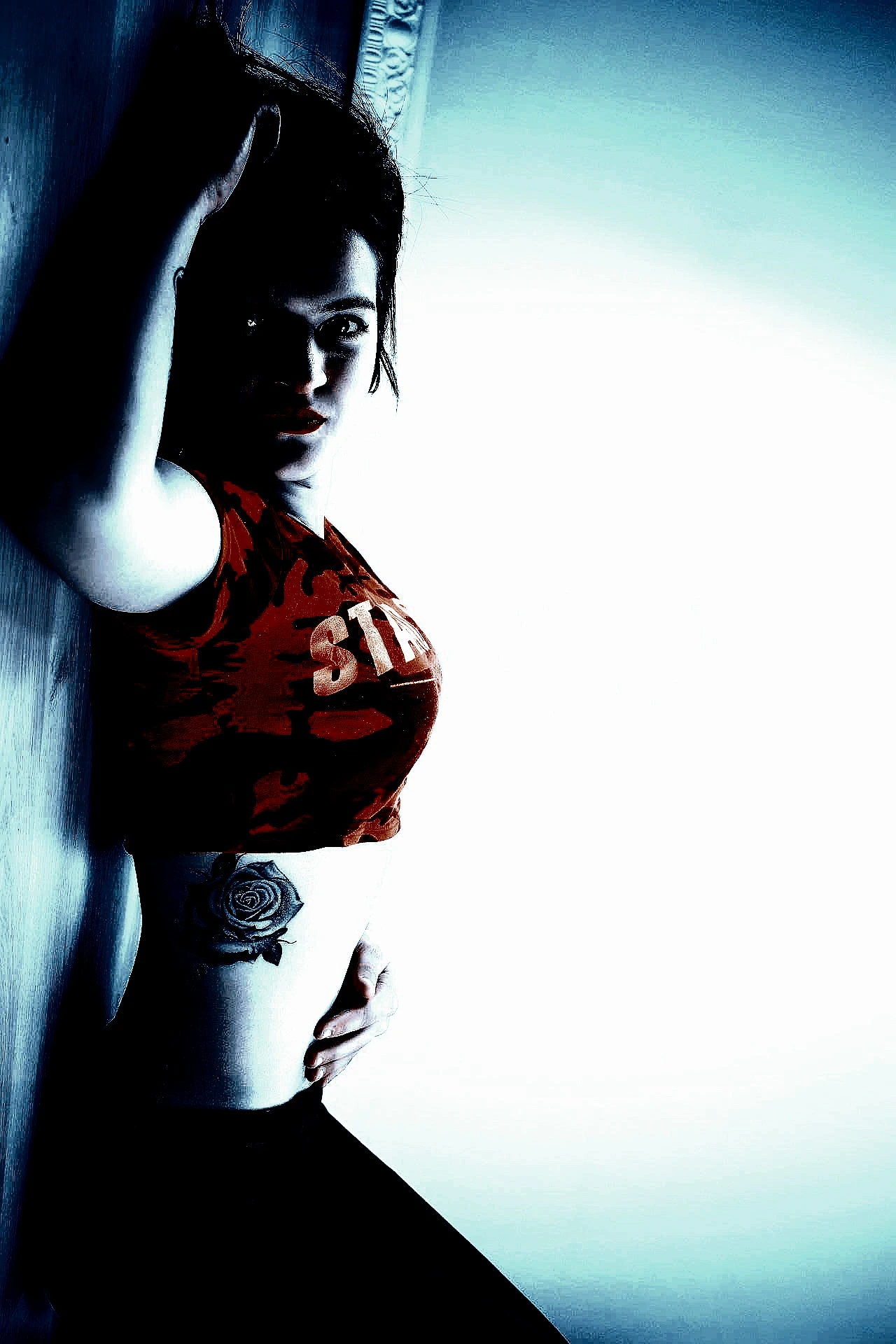 Metalhead tattoed woman with a red crop top posing up against the wall.