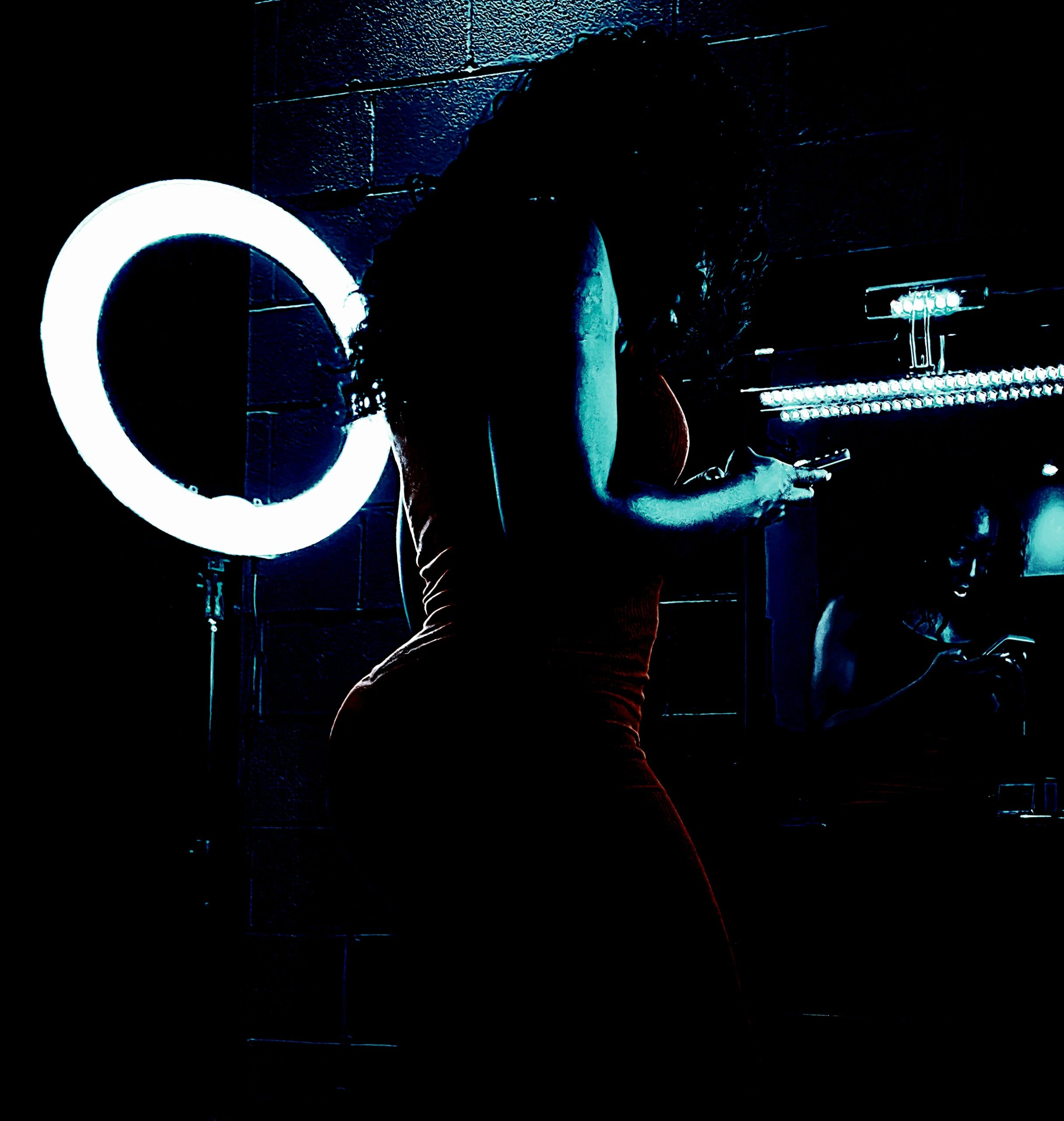 Silhouette of a woman in a tight dress using her phone, illuminated by a ring light, in front of a mirror.