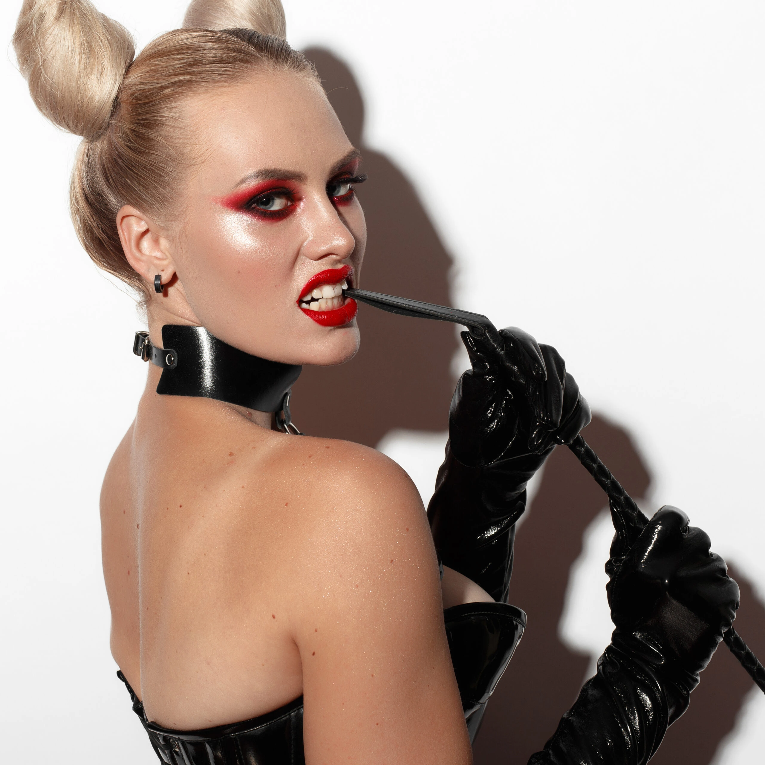 Model in a black latex bodysuit and leather corset holding a riding crop, showcasing dominatrix fashion. Ultimate Guide to Dominatrix Fashion.
