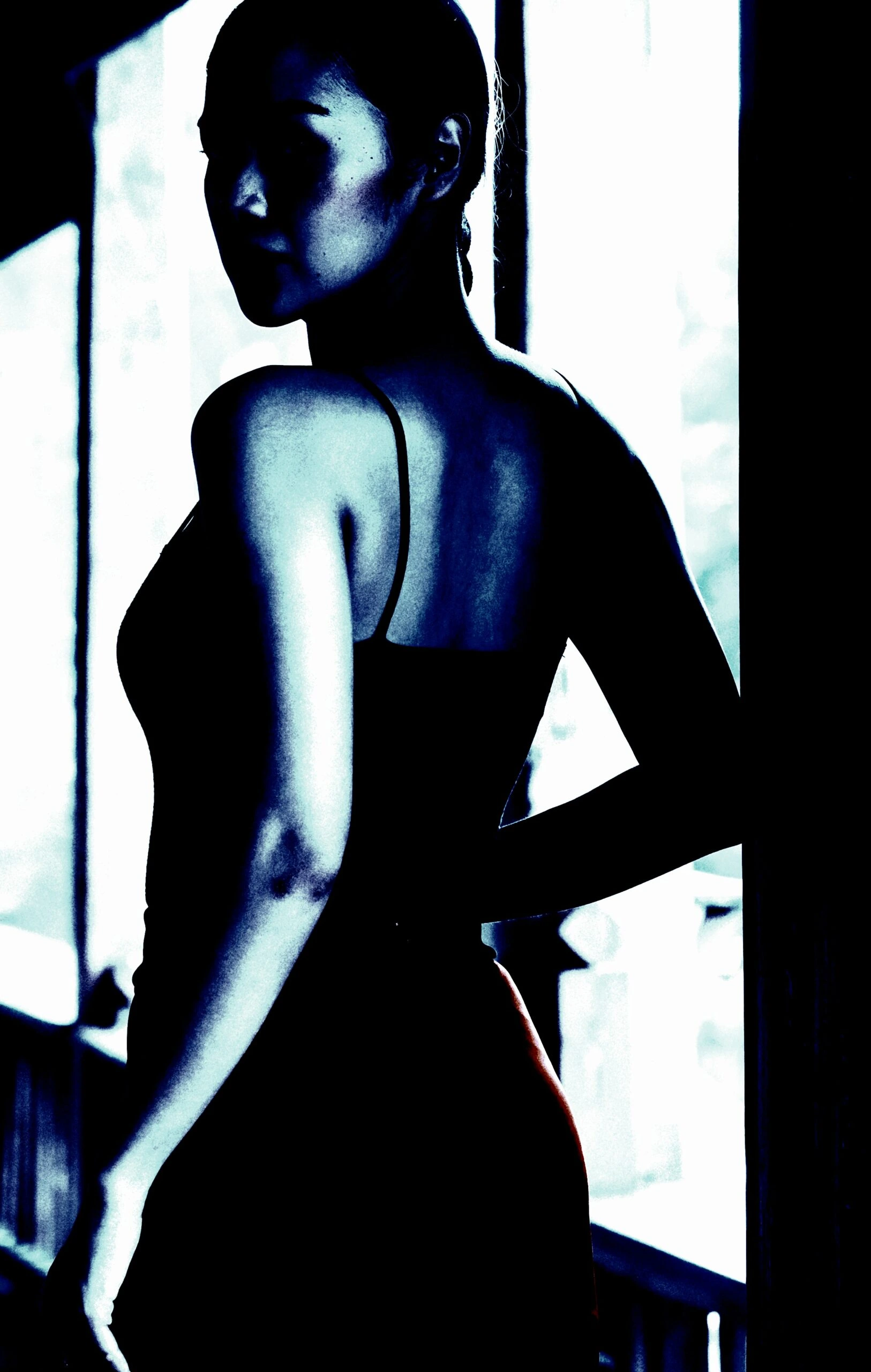 Navigating Sexuality in the Underground Music Scene: A woman seen from behind, standing by a window, highlighted by natural light that contours her silhouette.