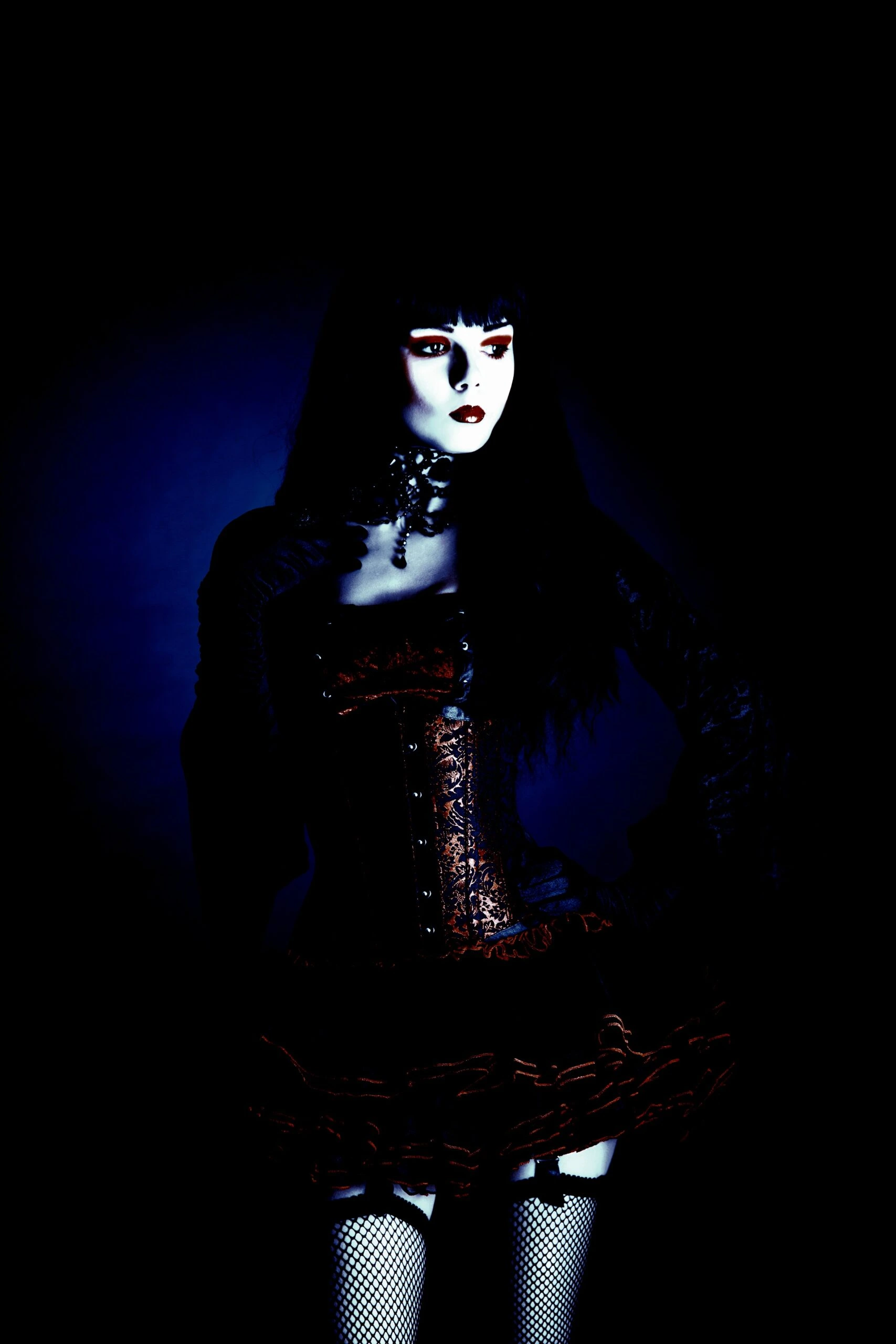 Elegant gothic model in a dark, romantic outfit featuring a corset and lace, highlighted by blue ambient light.