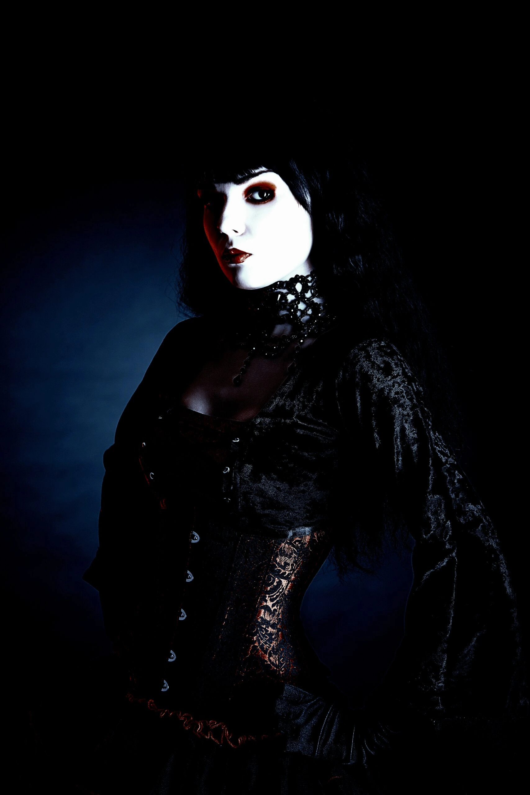 Portrait of a gothic woman with dramatic makeup, wearing a dark velvet corset and lace neckpiece.