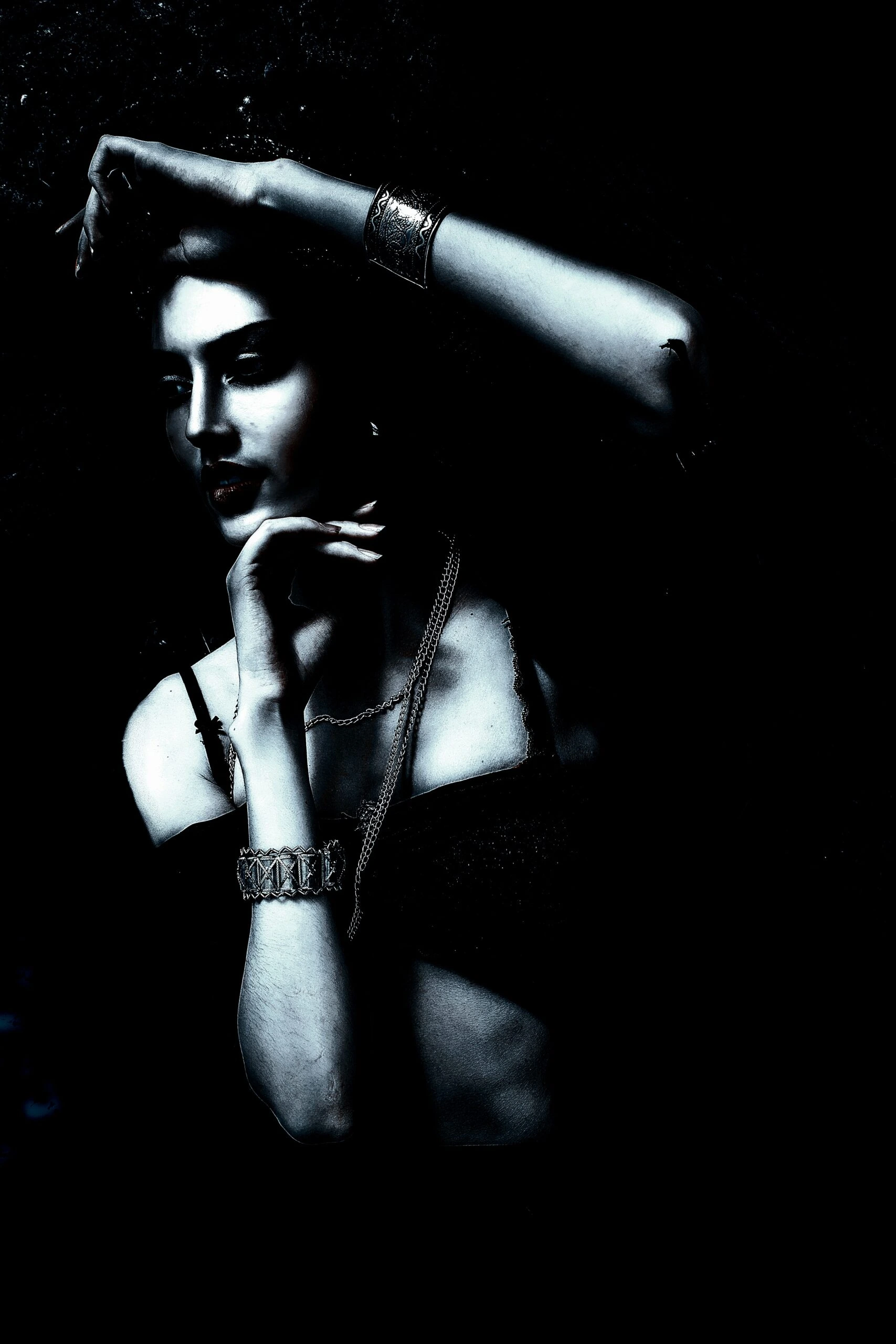 Mysterious woman wearing Gothic jewelry with moon phases and rings, surrounded by darkness.