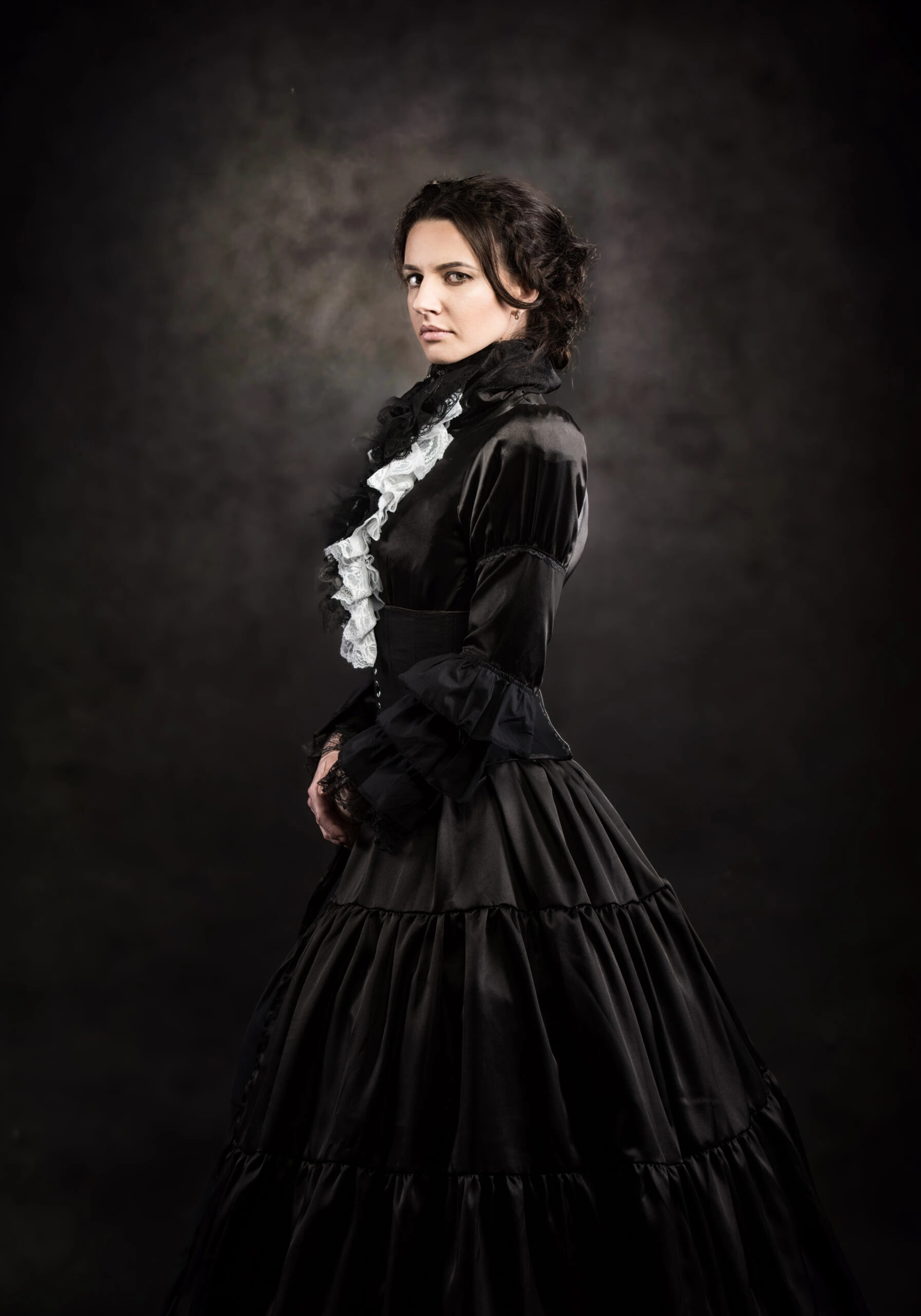 A woman posing in an elegant black Victorian dress with ruffled white details, giving the camera a pensive look.