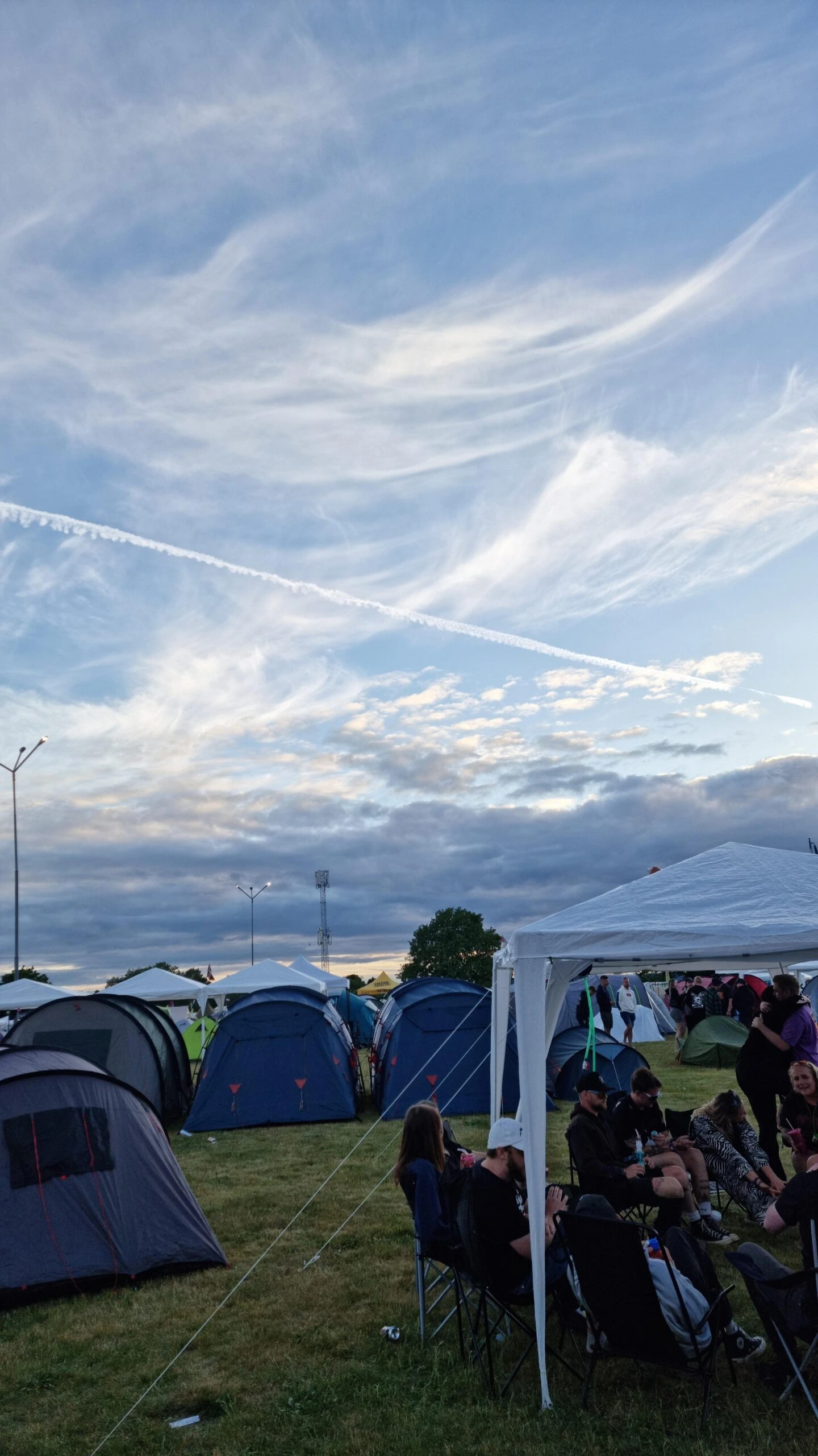Campsite with tents and people sitting under a canopy at Sweden Rock Festival 2024 during sunset