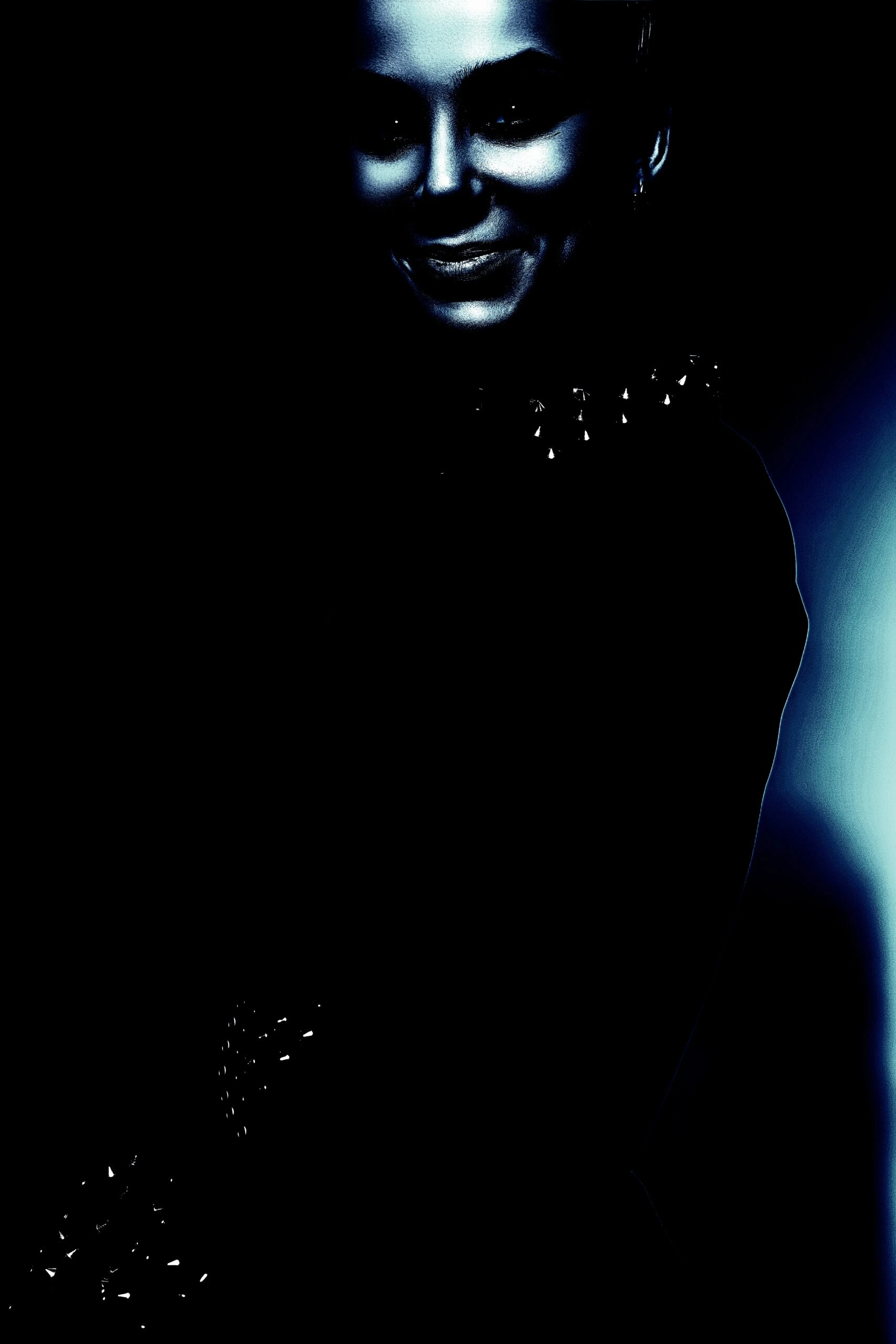 A gothic woman smiling enigmatically in a dark outfit adorned with studded spikes, against a dark background with a blue glow.