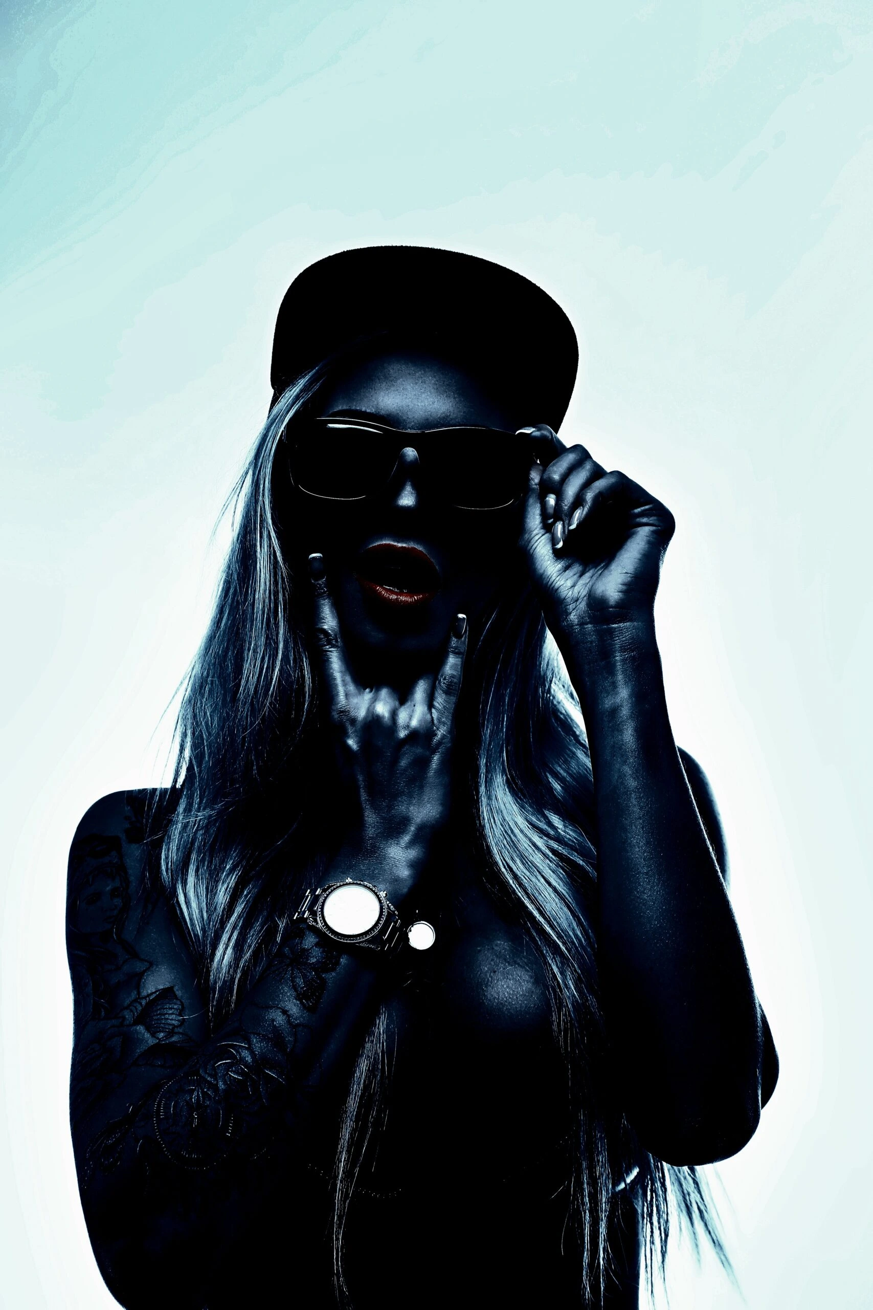 Tattooed lady in an alternative subculture making a rock sign with her hand and wearing sunglasses.