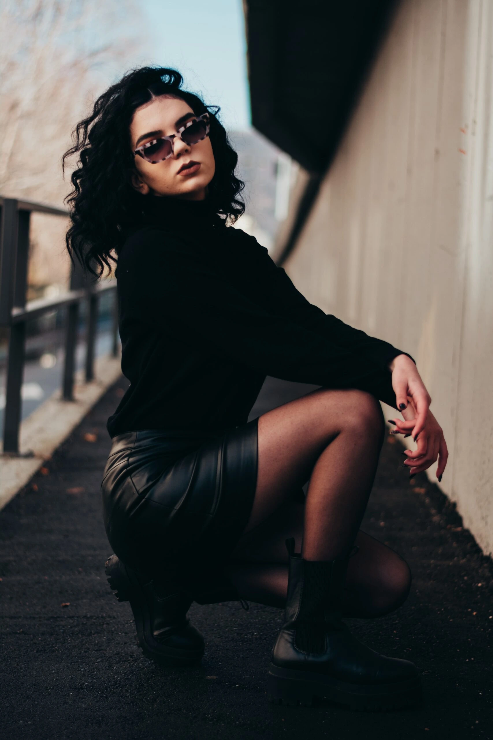 Curly-haired woman in black outfit and sunglasses, posing in an urban setting, highlighting the practicality of wearing sunglasses at night.