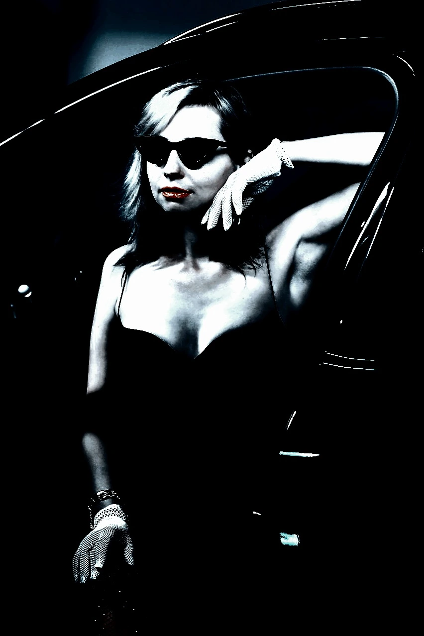 Woman with braided hair and black sunglasses looking upwards in a high-contrast, dark-themed photo.