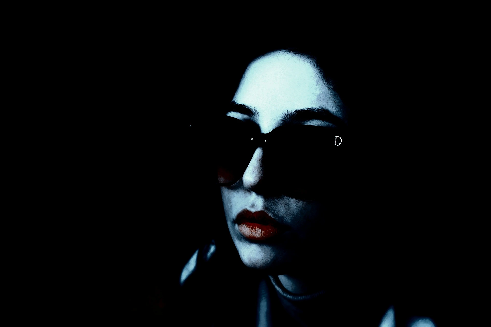 Woman sitting on a rooftop wearing sunglasses and a casual outfit, with a dark and moody atmosphere.