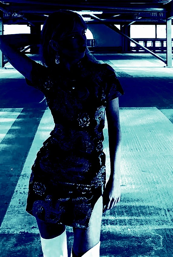 Woman wearing a short goth summer dress with dragon patterns, posing in a dark, empty parking garage.
