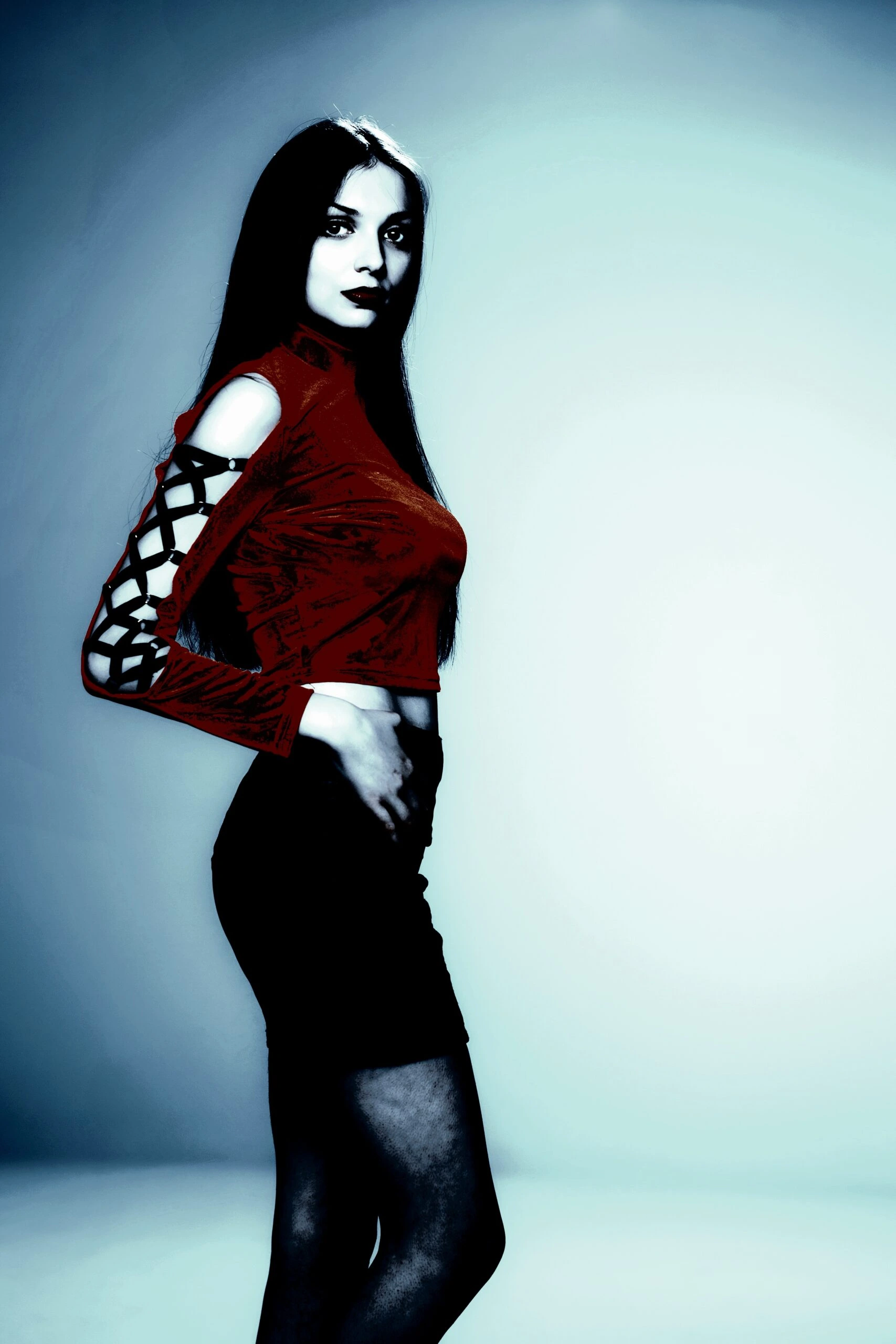 Gothic woman in a red top with lattice sleeves, standing confidently against a light background.
