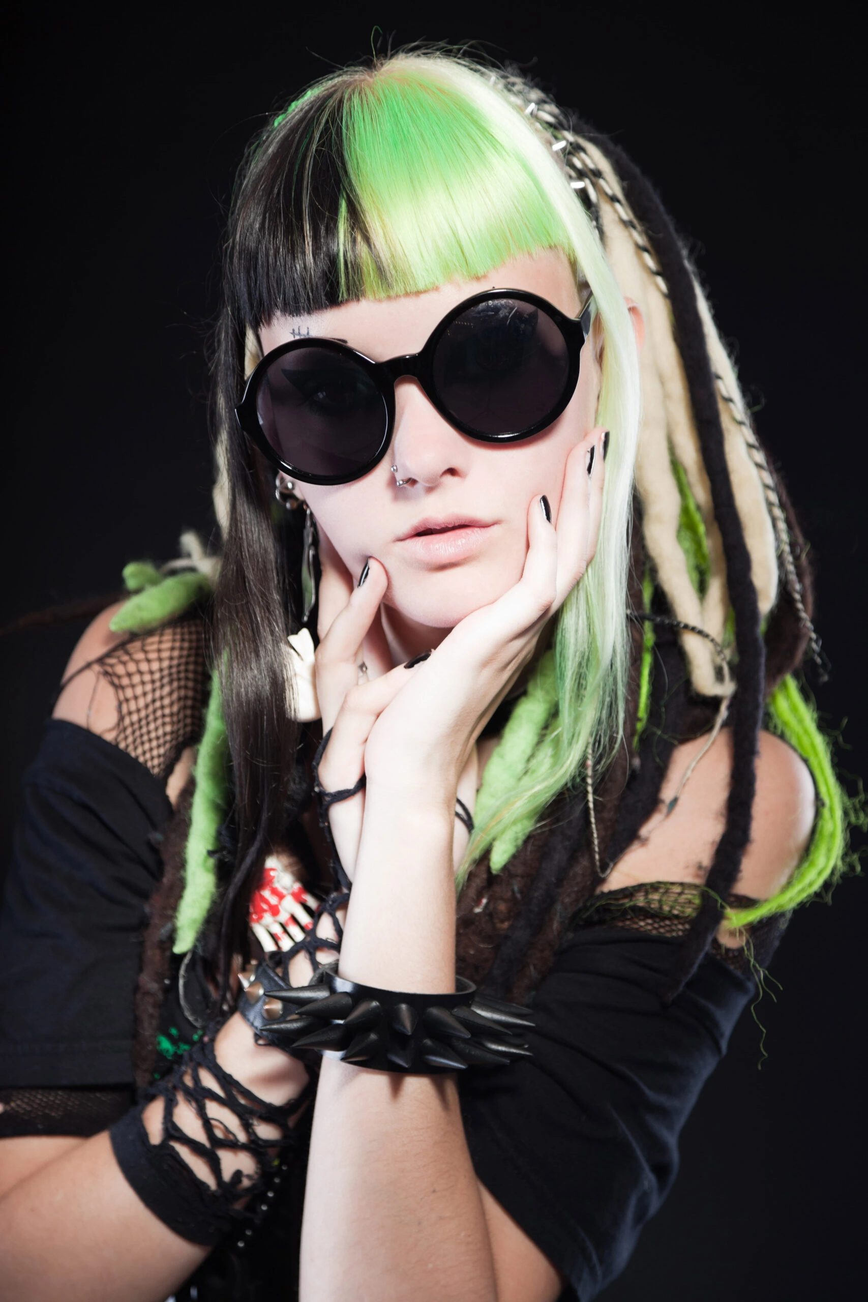 Alternative fashion woman with green and black hair wearing round sunglasses, showcasing the edgy style of wearing sunglasses at night.