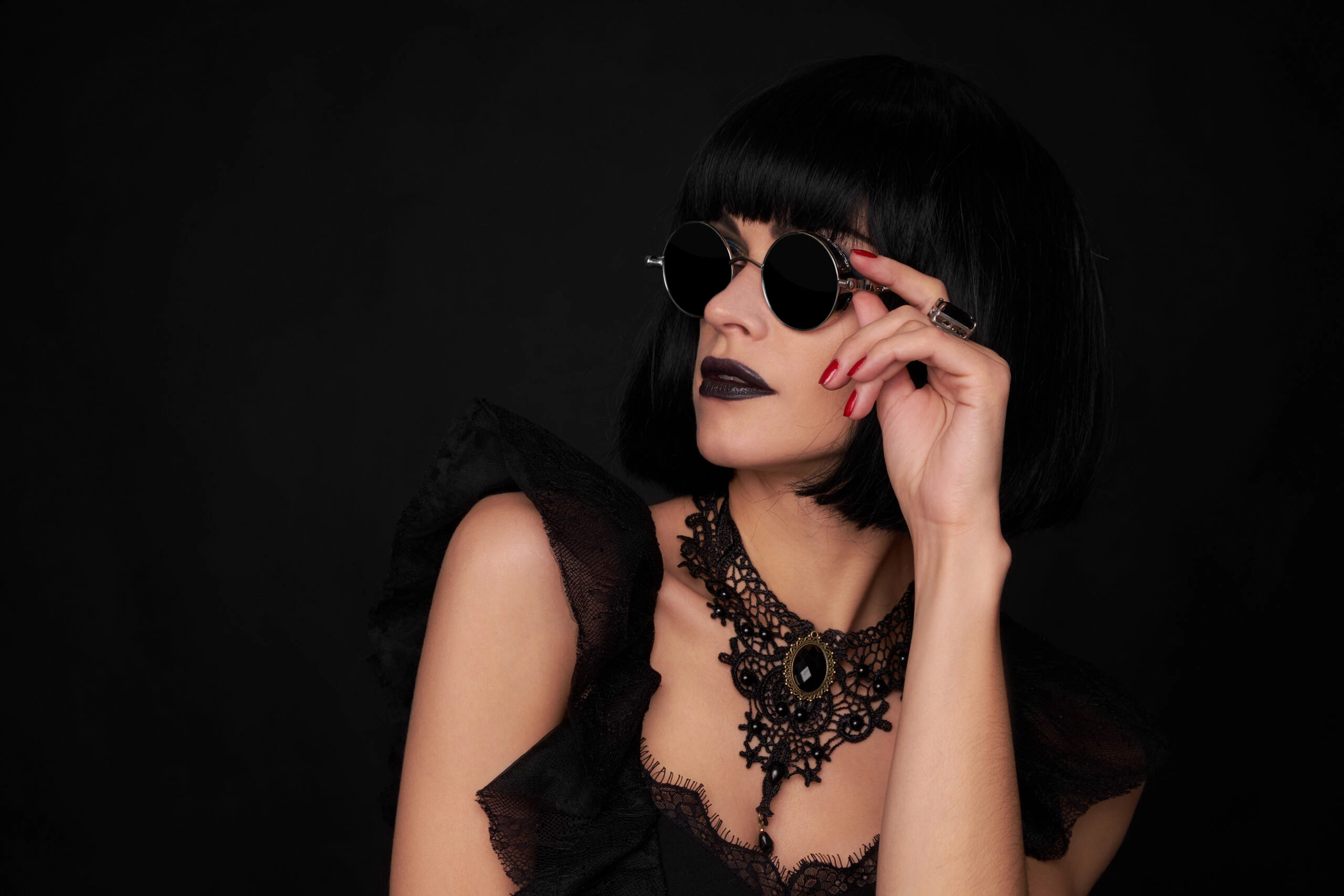 Woman in gothic attire with round sunglasses, emphasizing the bold fashion statement of wearing sunglasses at night.
