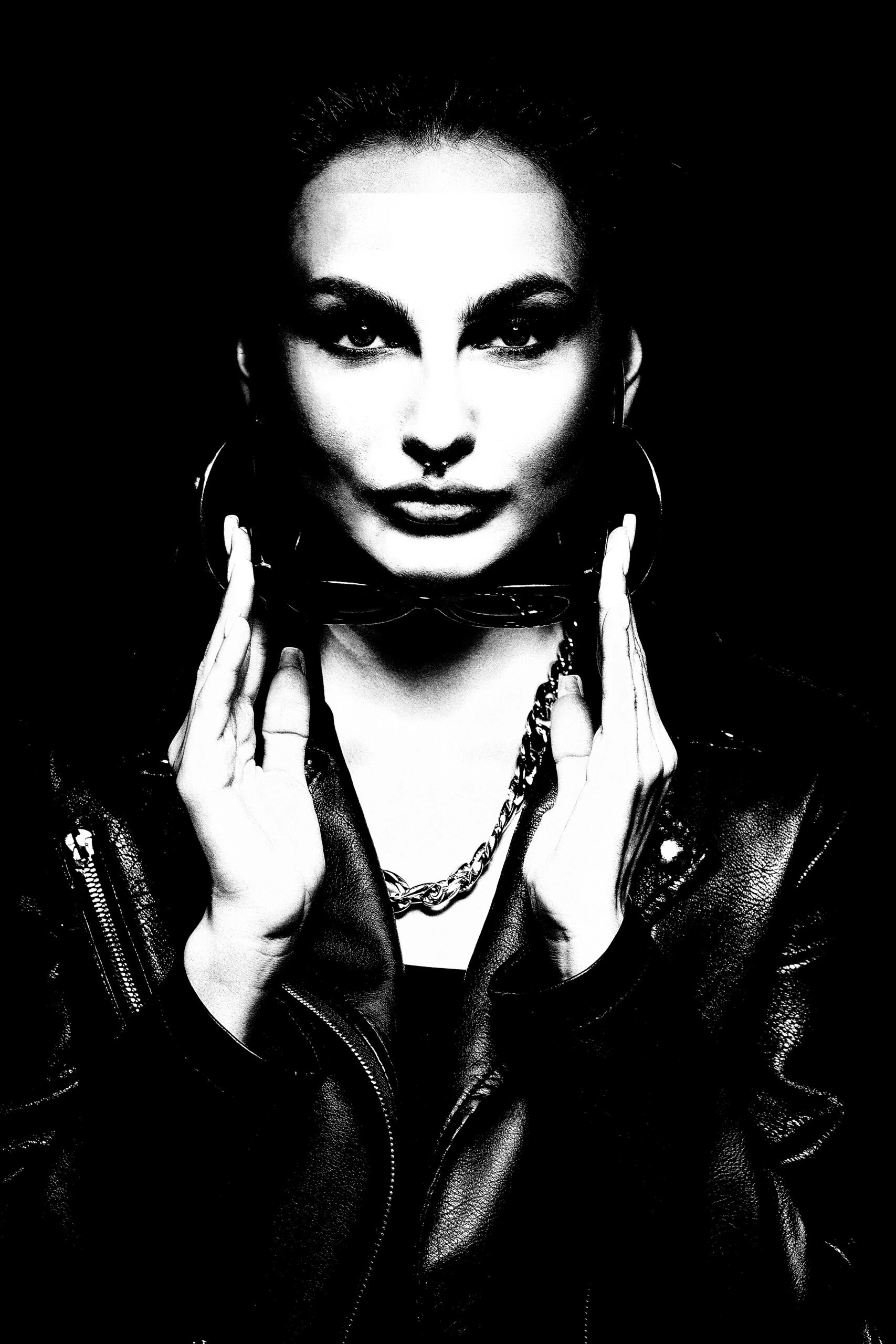 High-contrast black and white photo of a gothic woman wearing a leather jacket and holding sunglasses.