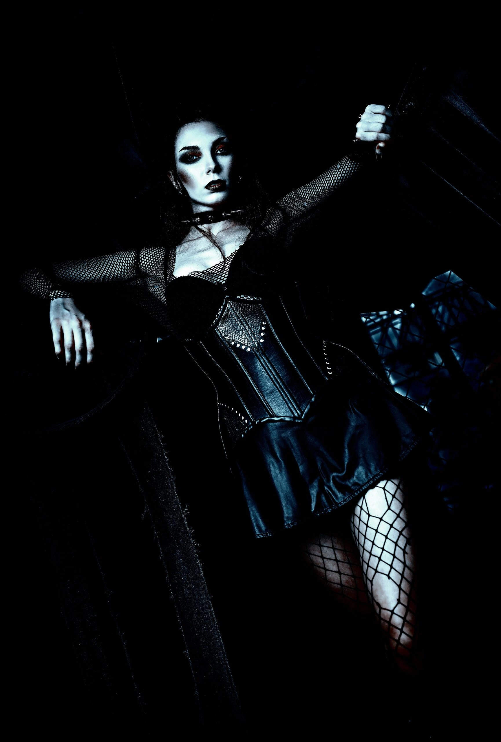 Gothic woman in a corset and fishnet stockings, posed dramatically in a dark setting.