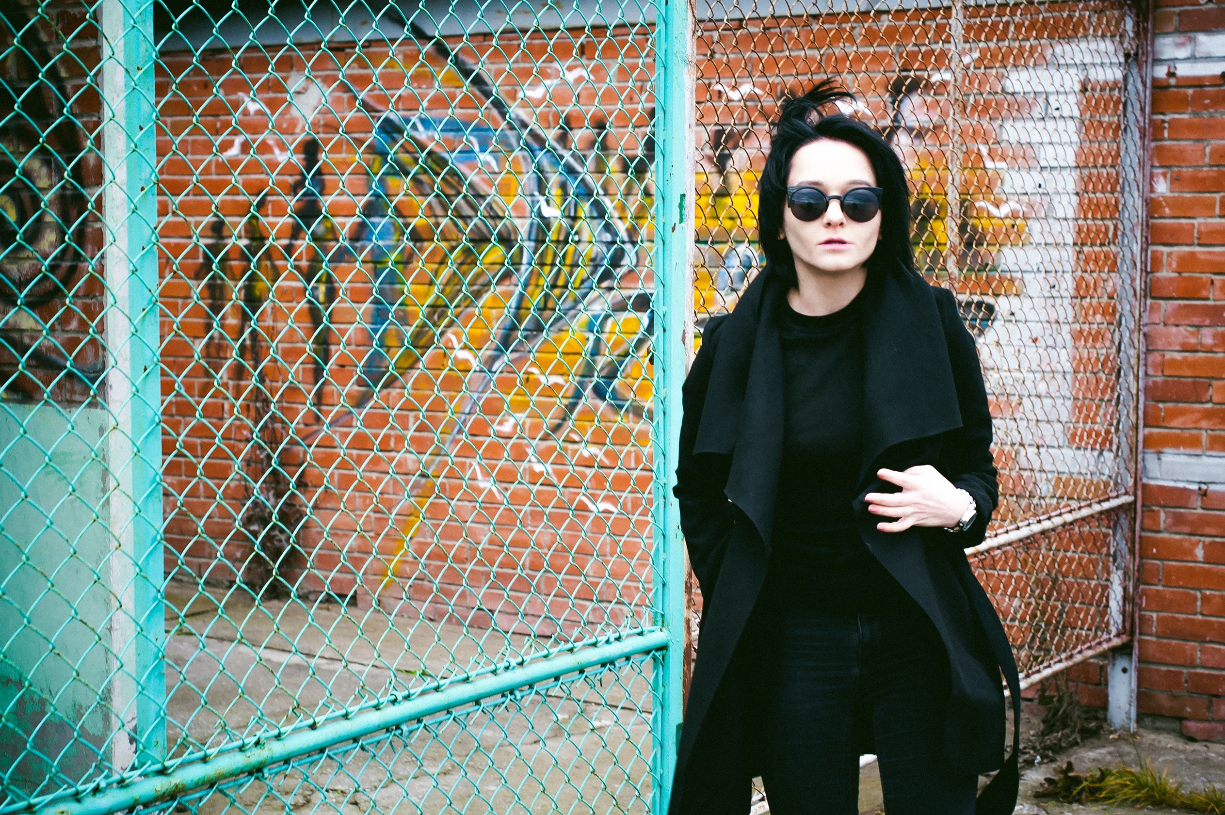 Two women in gothic attire and sunglasses, sitting against a wall, embodying the rebellious style of wearing sunglasses at night.