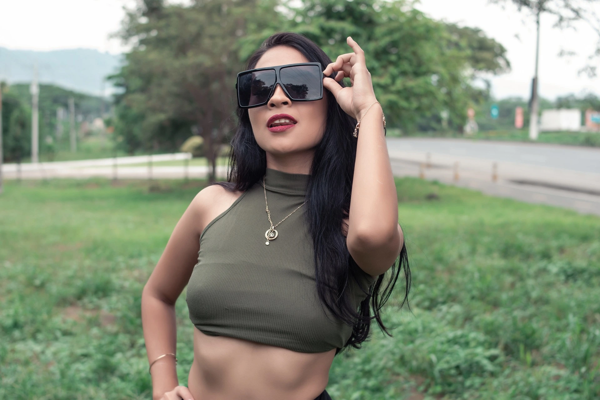 Stylish woman in a crop top and large sunglasses, confidently posing outdoors, illustrating the trend of wearing sunglasses at night.