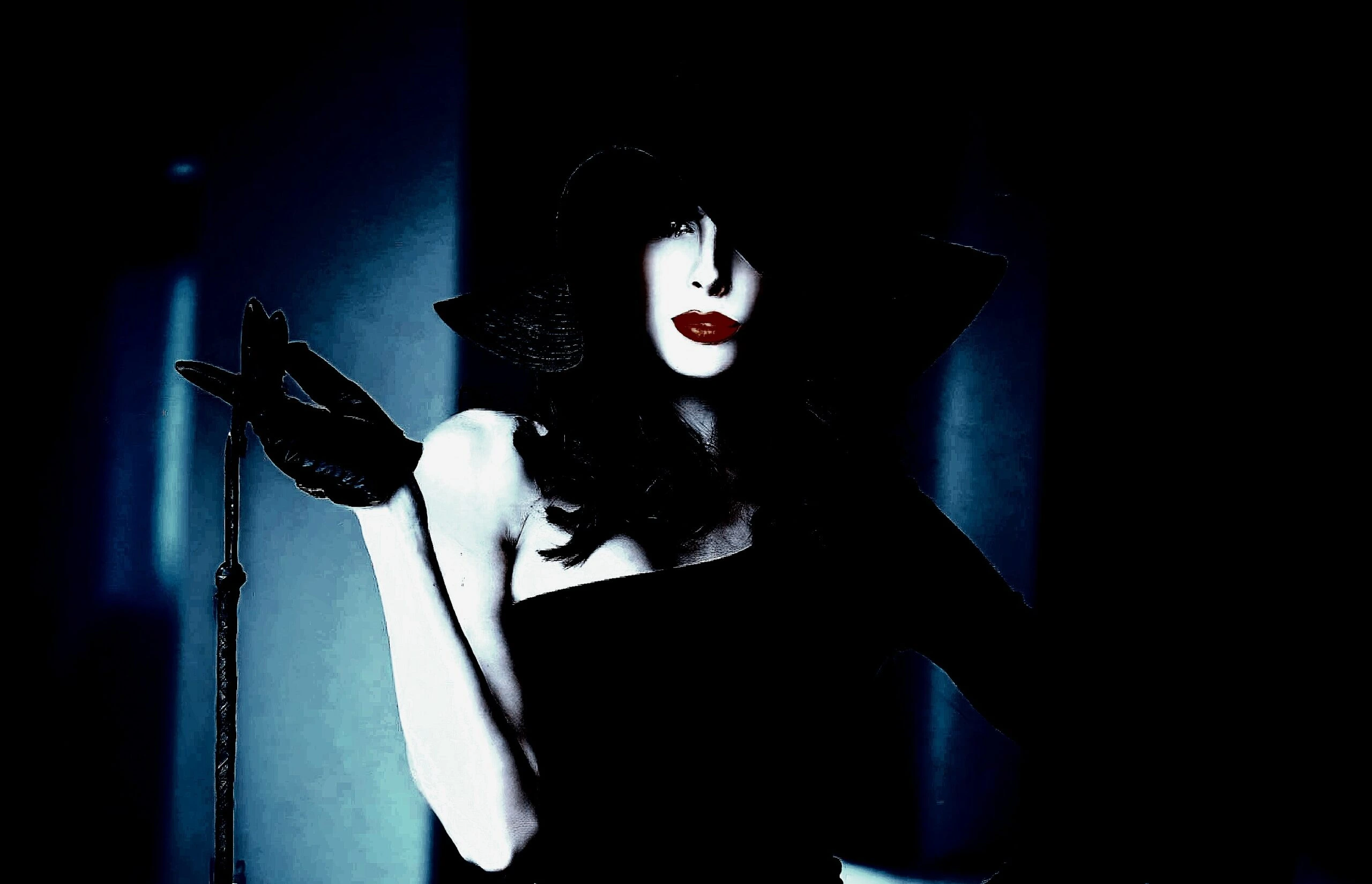 A woman with dark hair and dramatic makeup, dressed in a stylish, form-fitting outfit, exuding an air of sophistication and mystery.