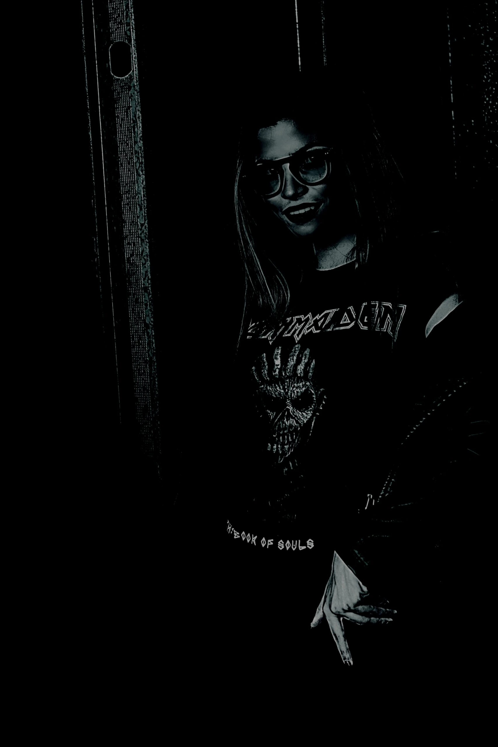 Goth woman wearing an Iron Maiden T-shirt standing in a dark setting.