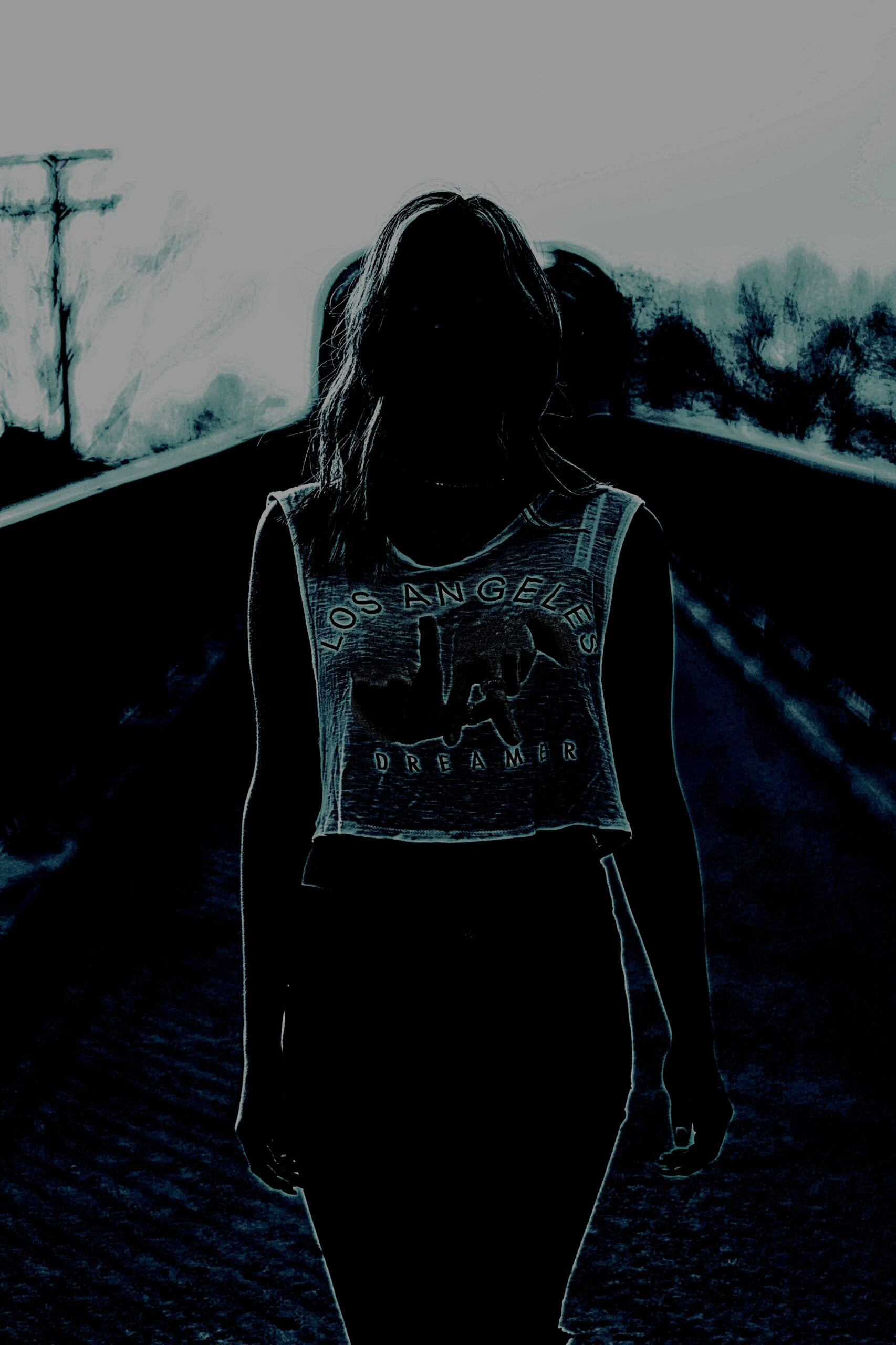 Silhouette of a woman standing on a bridge wearing a cropped Los Angeles Dreamer T-shirt.