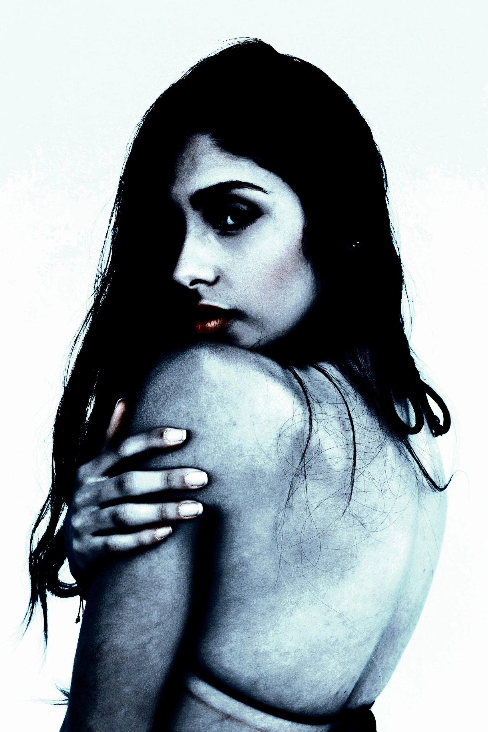 Woman with dark hair and a bare shoulder looking over her shoulder in a high-contrast photo.