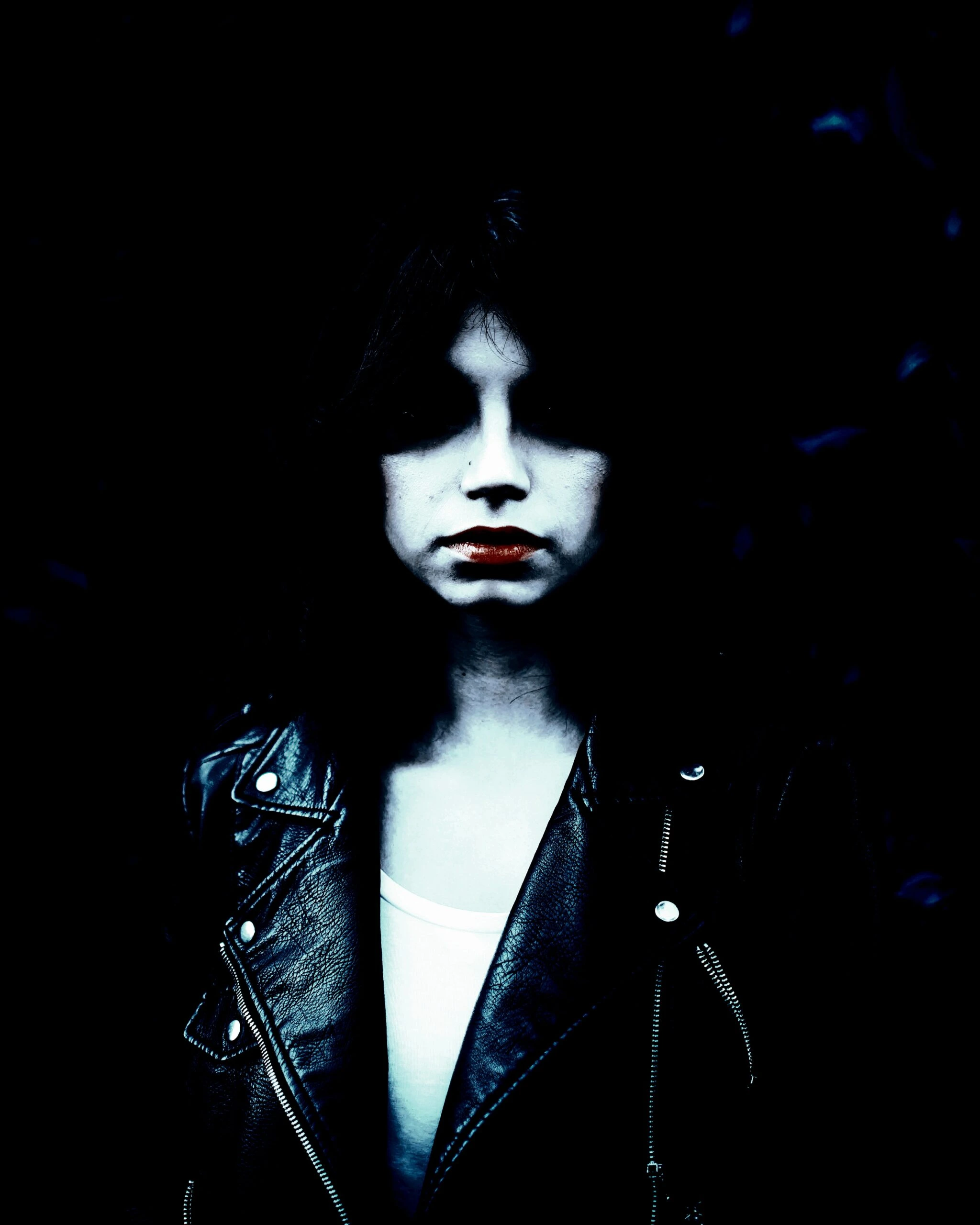 Portrait of a young woman with dark hair and a leather jacket standing against a dark, leafy background.