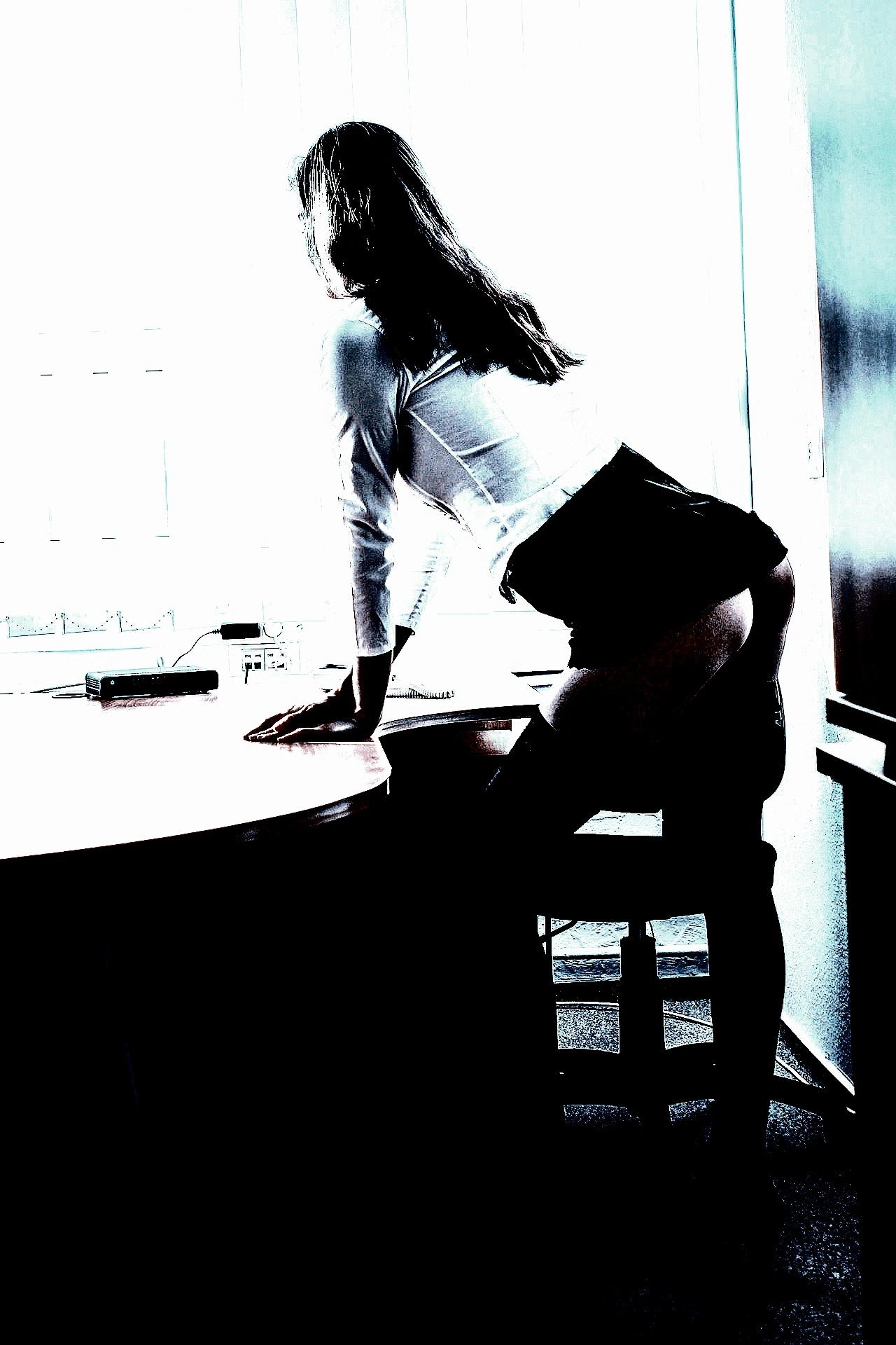 Silhouetted woman in office attire leaning over a desk in a high-contrast image.
