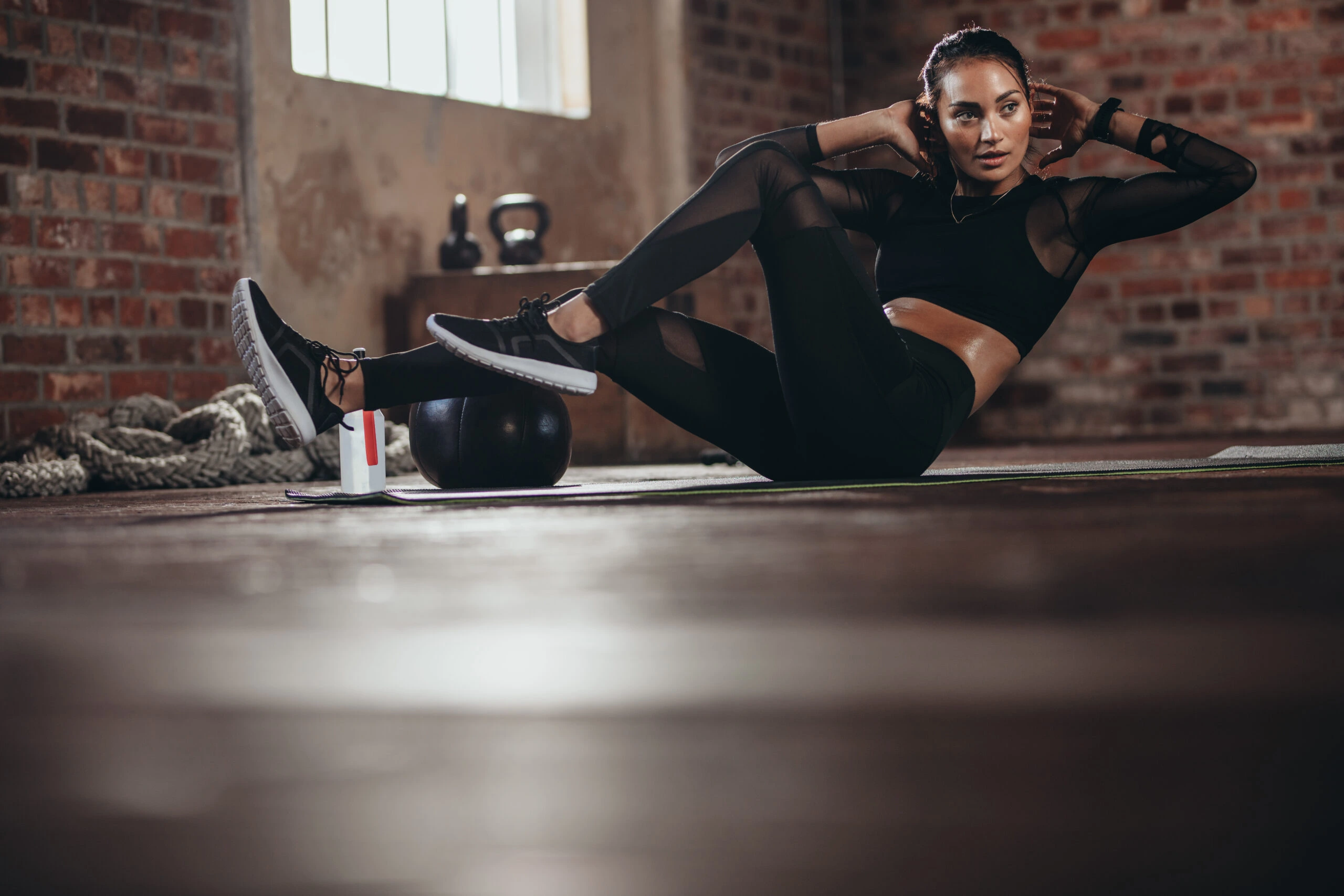 Woman in a dark gym performing ab exercises in a gothic-inspired workout outfit.