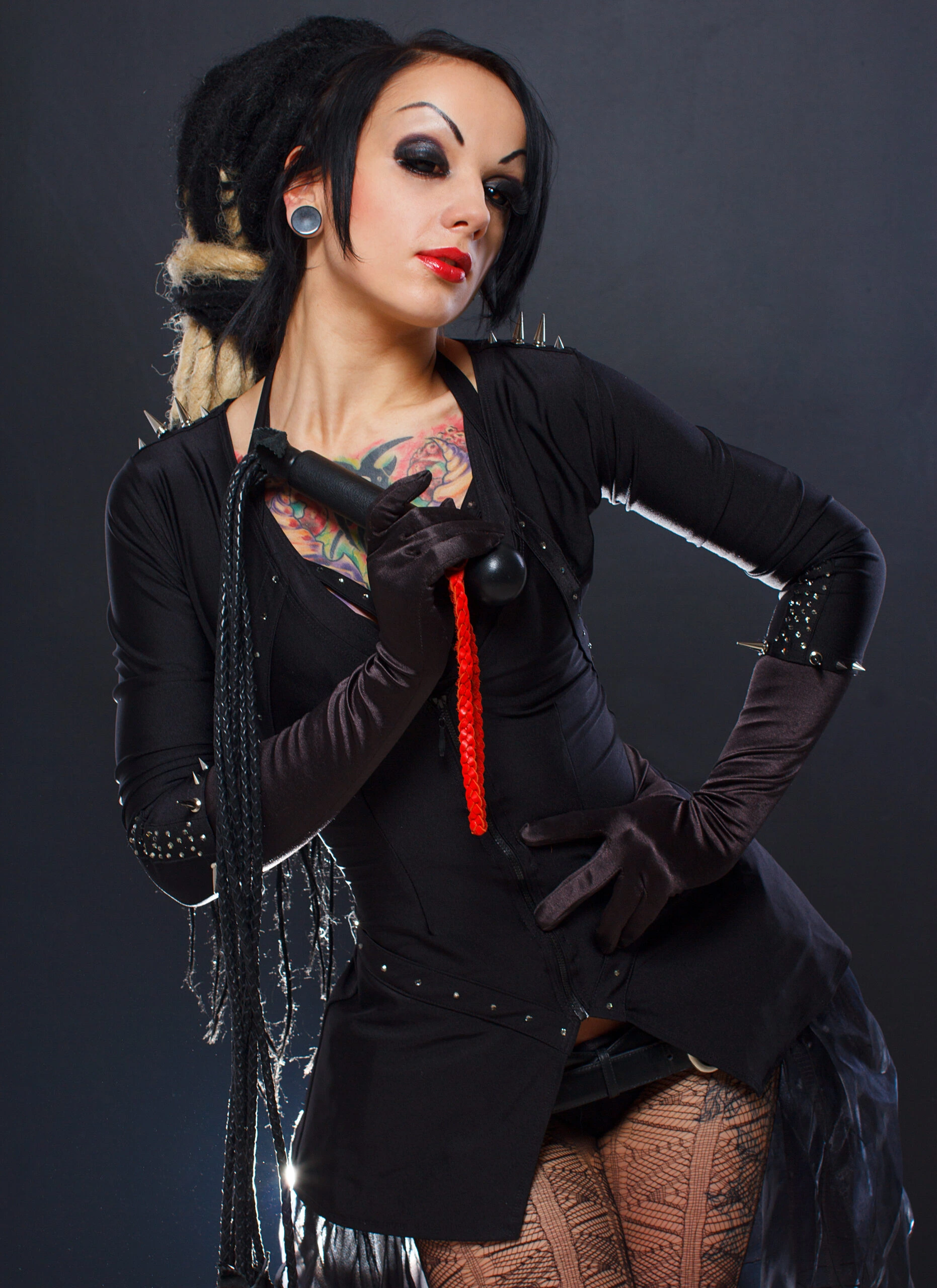 Gothic woman with dreadlocks wearing a black over bust corset and holding a whip. 