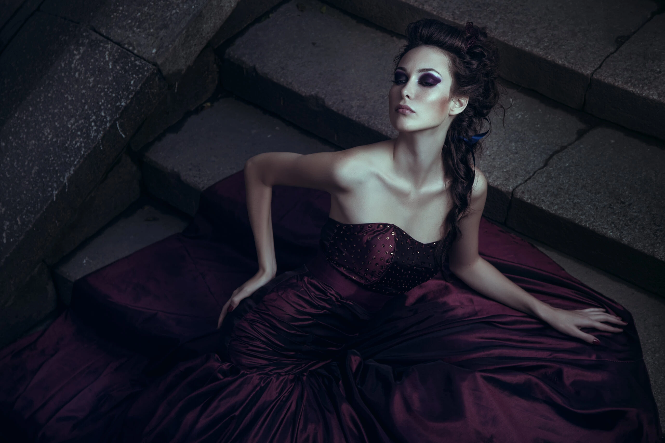 Gothic woman in a deep purple satin gown, reclining gracefully on stone steps in a dramatic, moody setting.