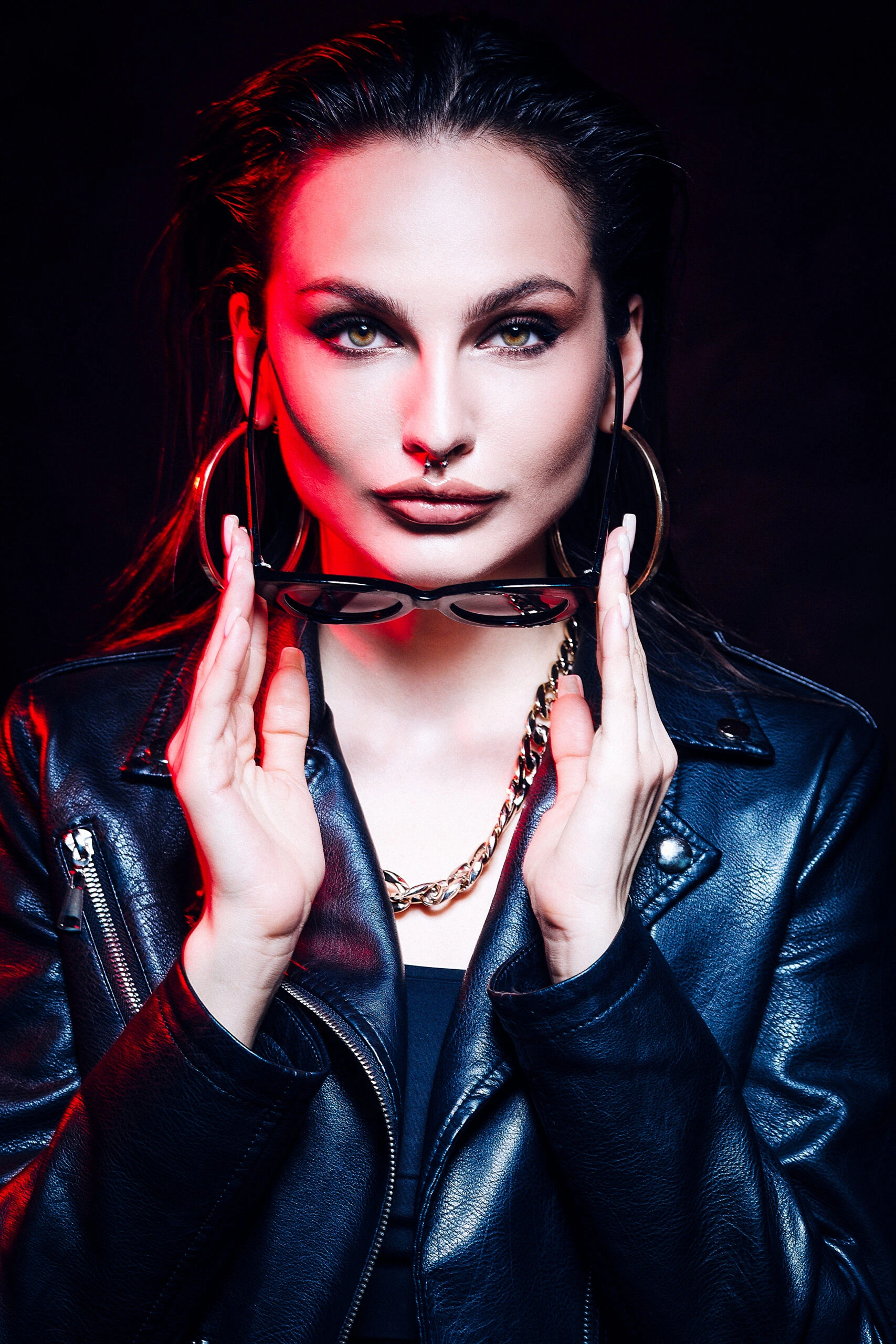 Woman in a leather jacket and bold Gothic makeup, holding sunglasses in a dramatic pose.