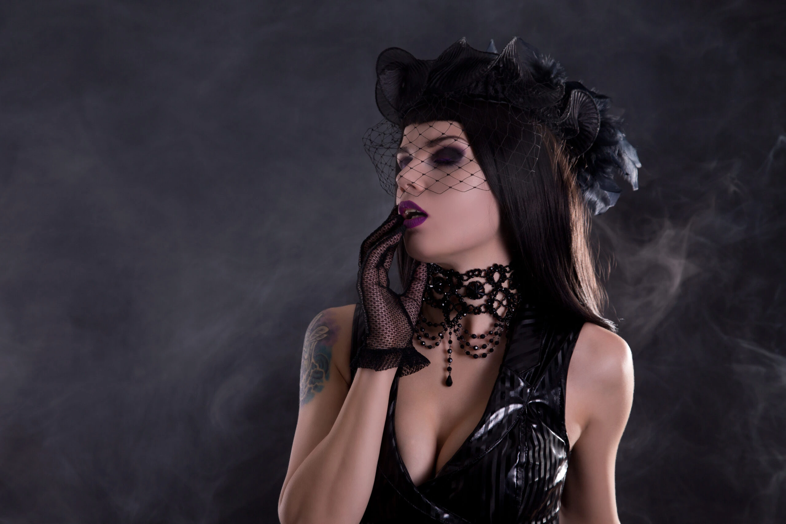 Gothic woman in a black veiled fascinator, looking contemplative with a dark, smoky background.