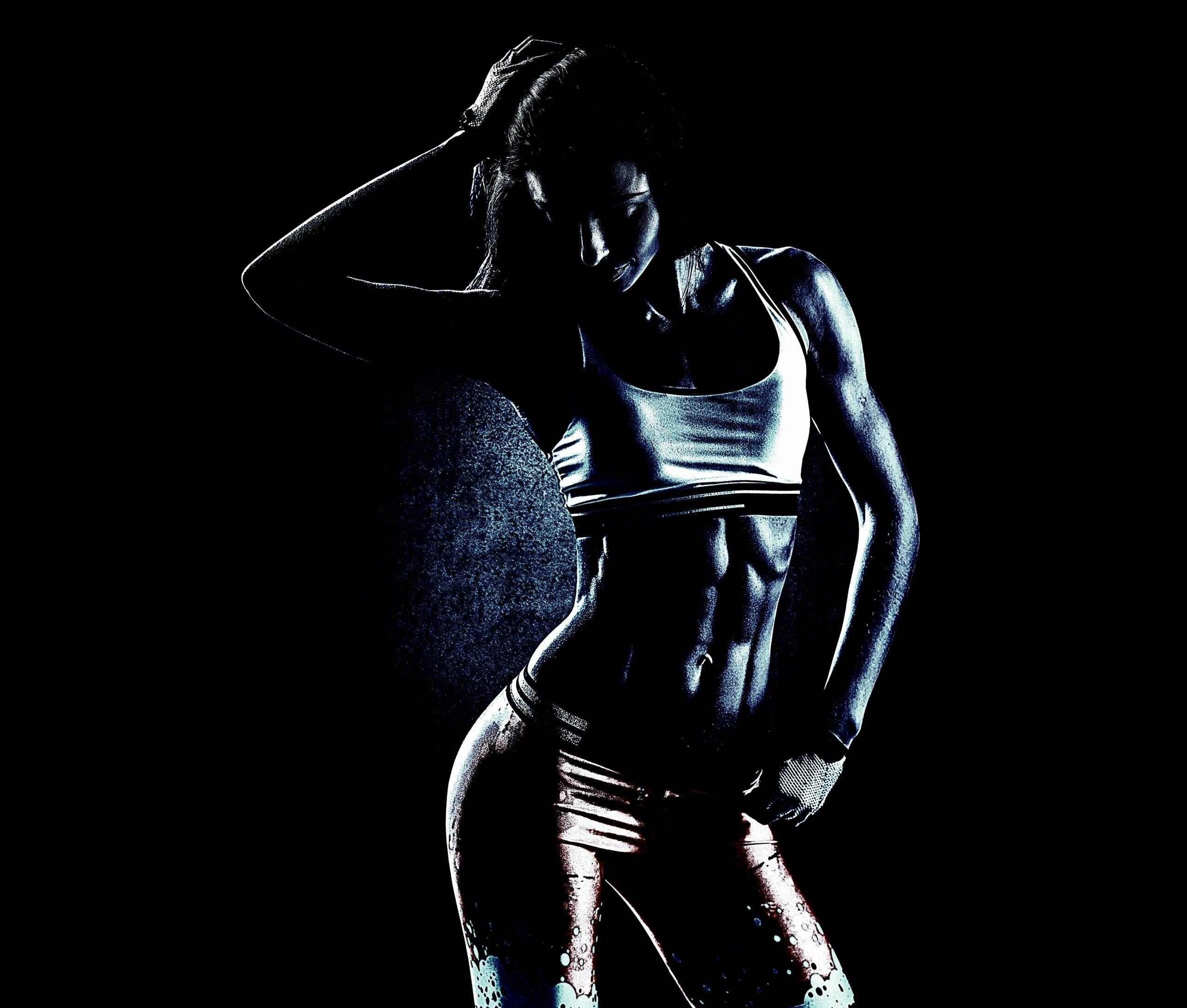 Silhouette of a fit woman posing in a dark gym, showcasing her toned abs and muscles.