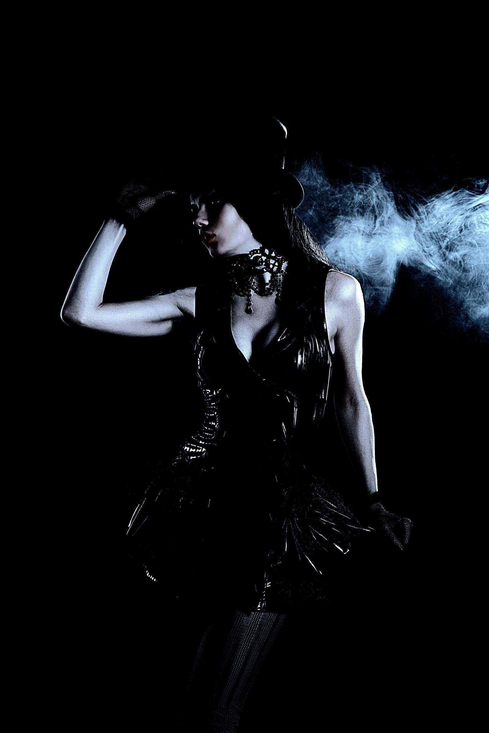 Elegant goth woman in a black corset, wearing a top hat, with a smoky atmosphere and low lighting.