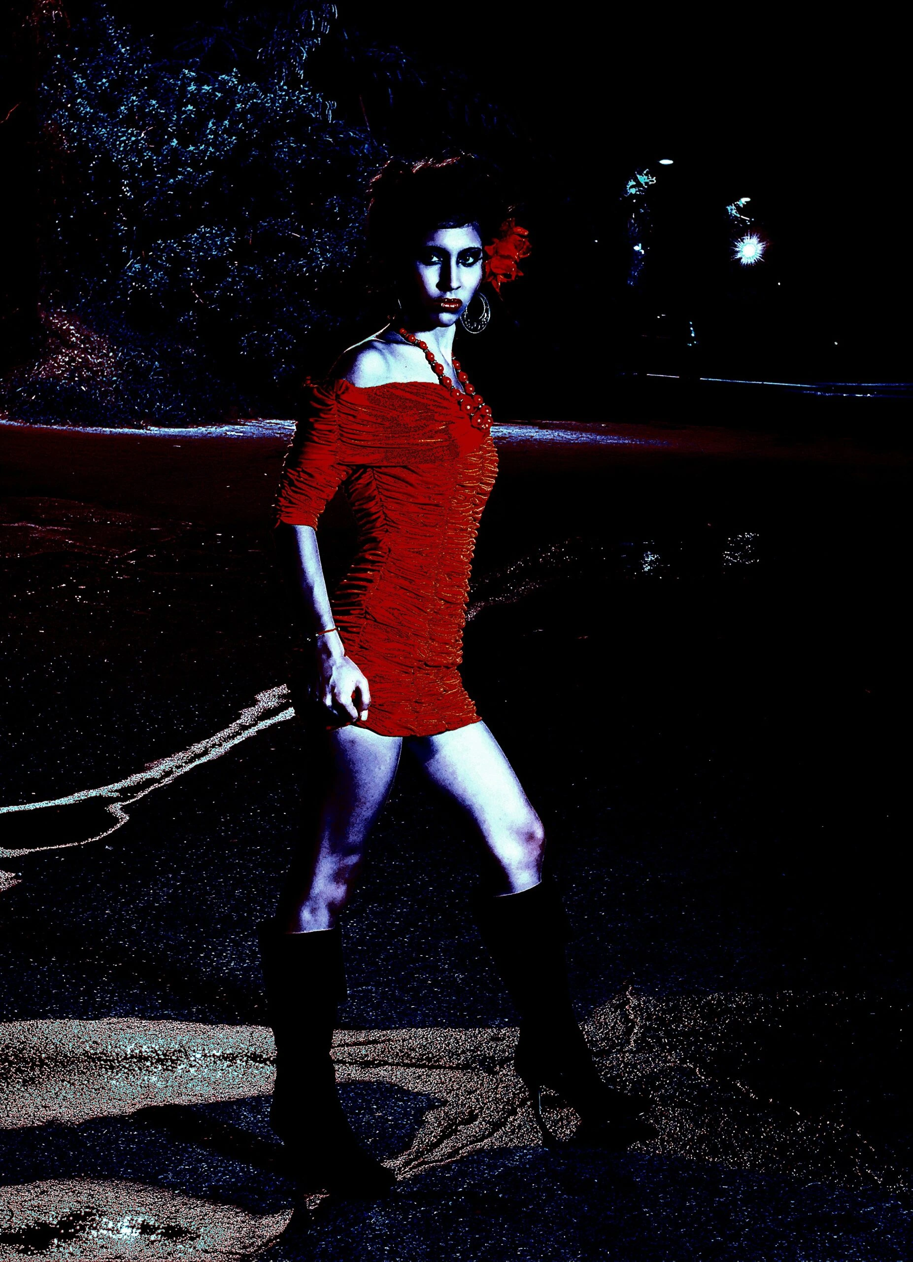 Woman in a red dress walking confidently at night, with a flower in her hair and a determined expression.
